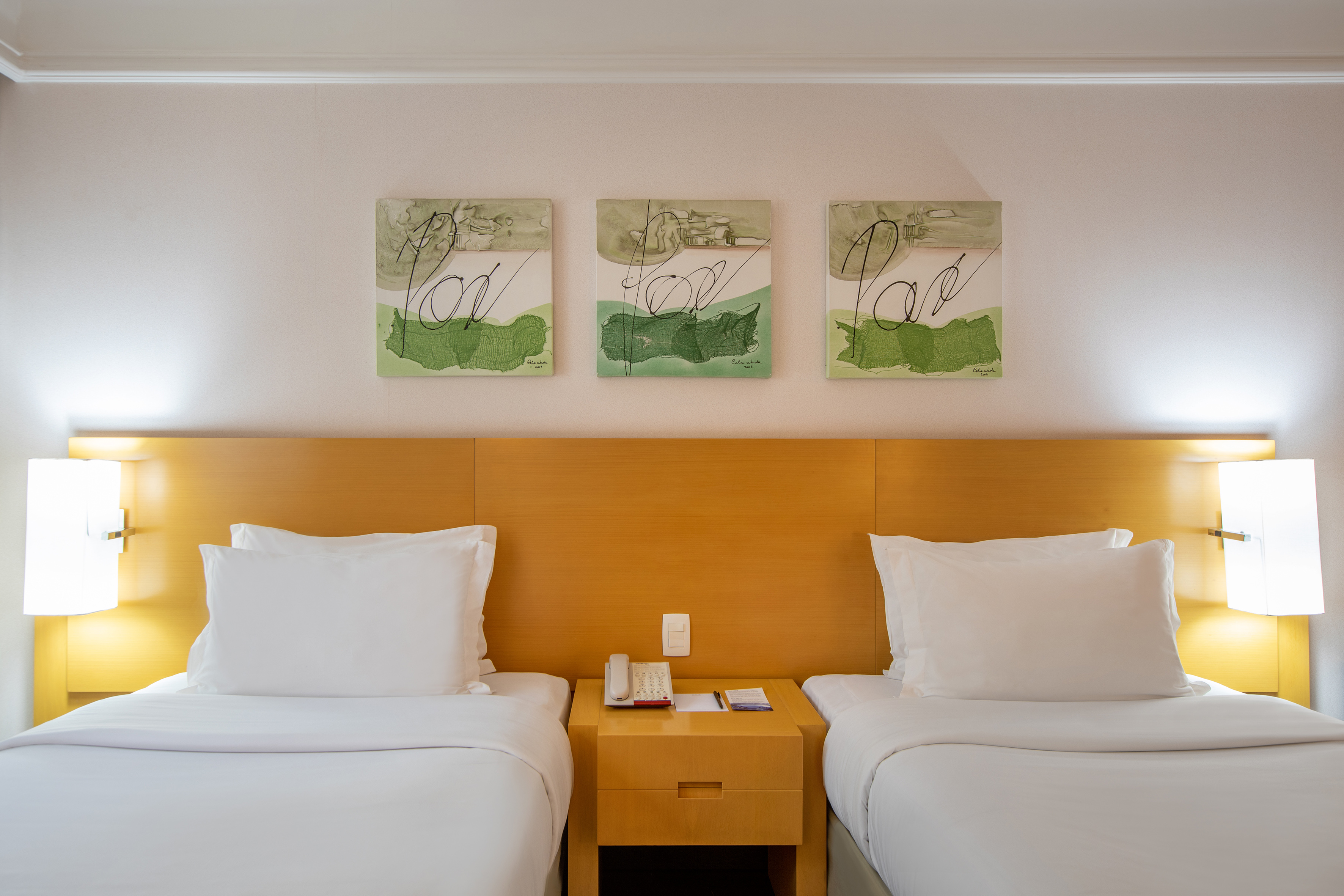Hotel room with twin beds, white bedding, wooden headboard, green abstract art.