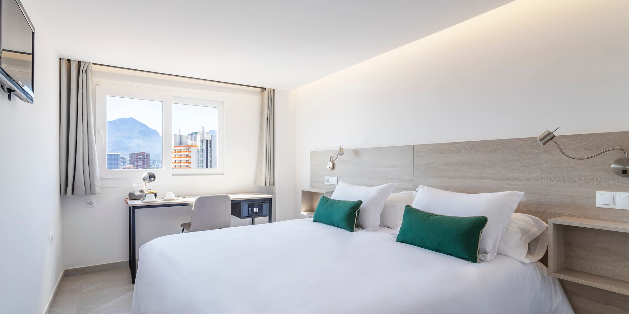 a bed with white sheets and green pillows in a room with a window