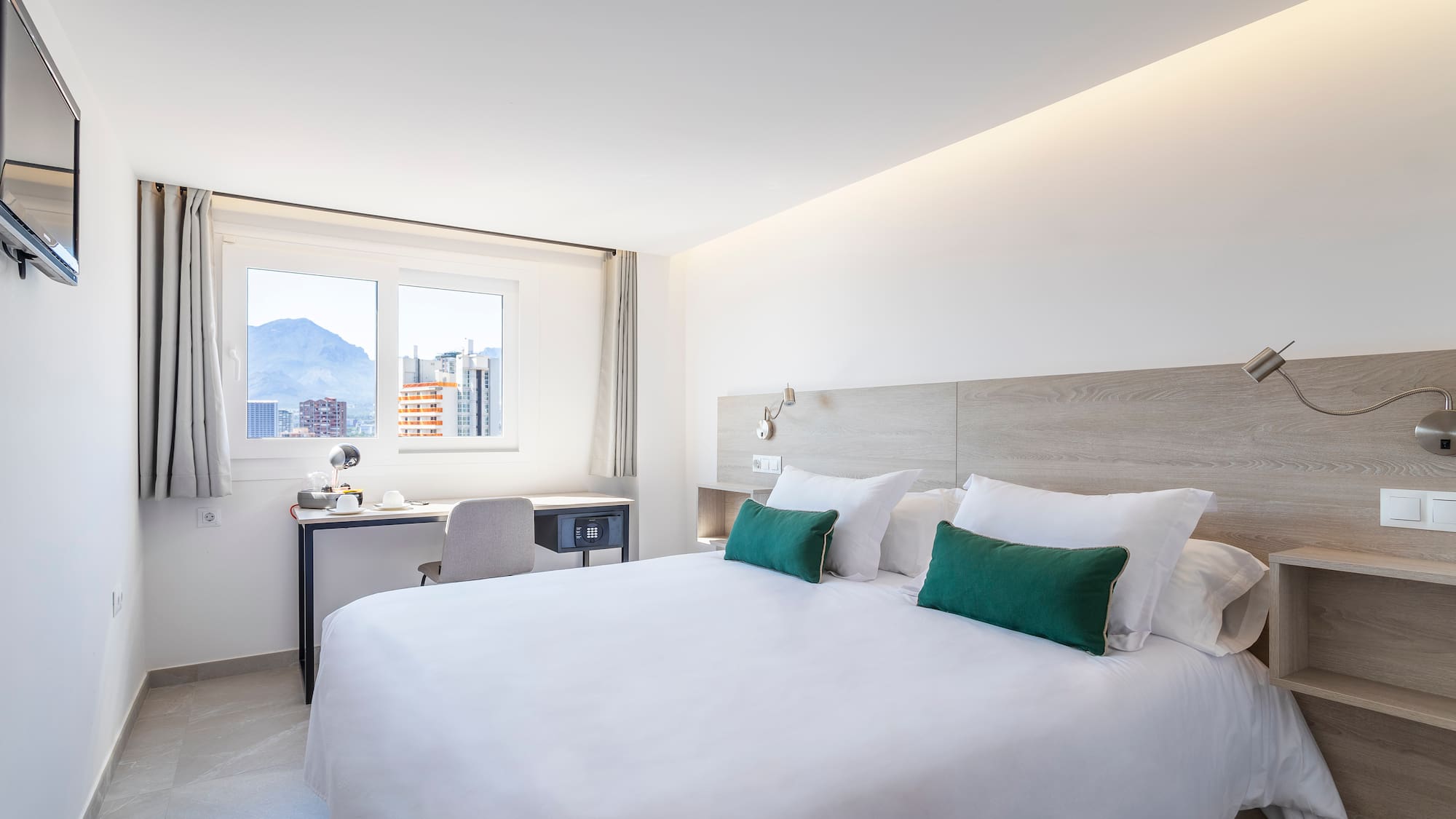 Bright modern hotel room with queen bed, desk, and mountain city view.