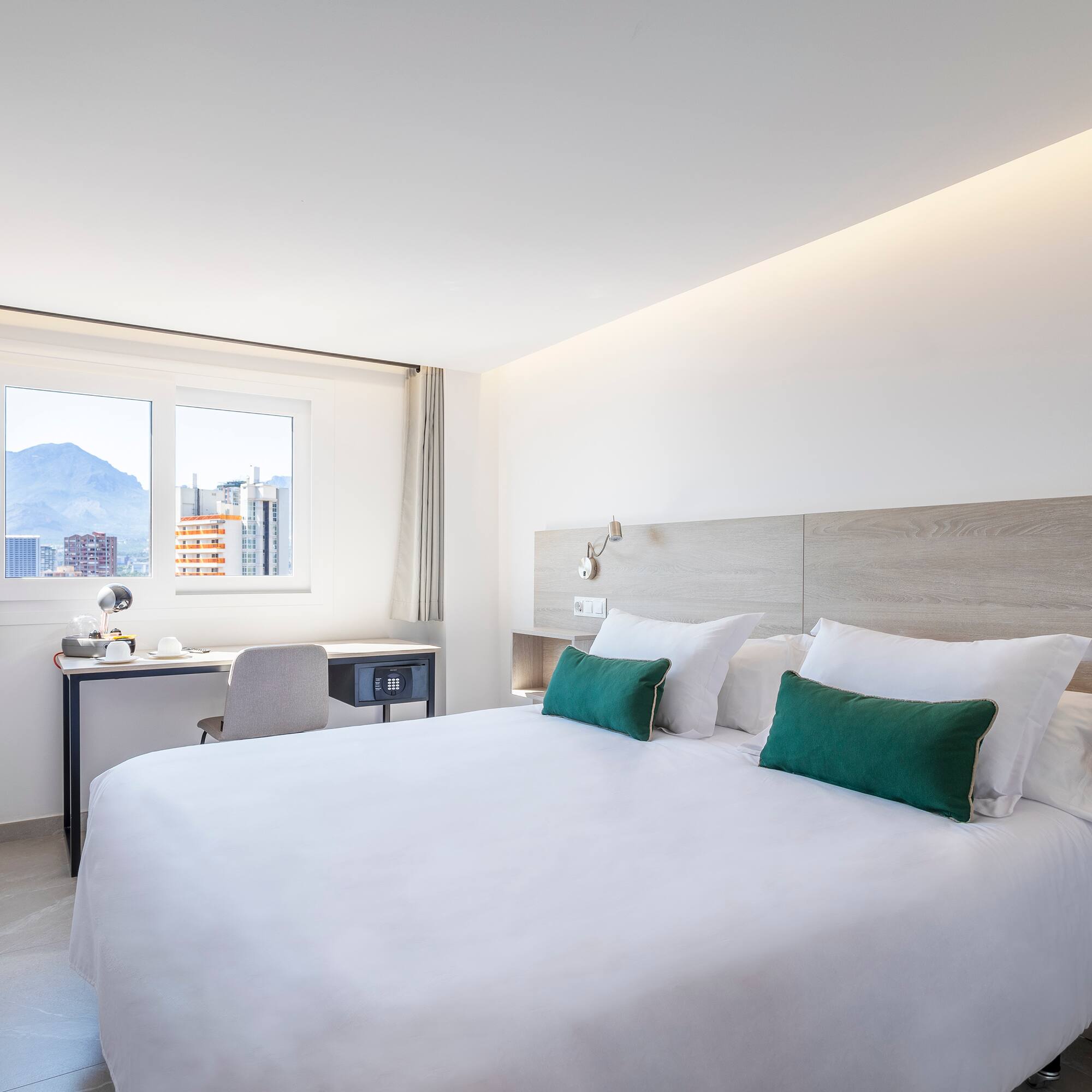 a bed with white sheets and green pillows in a room with a window