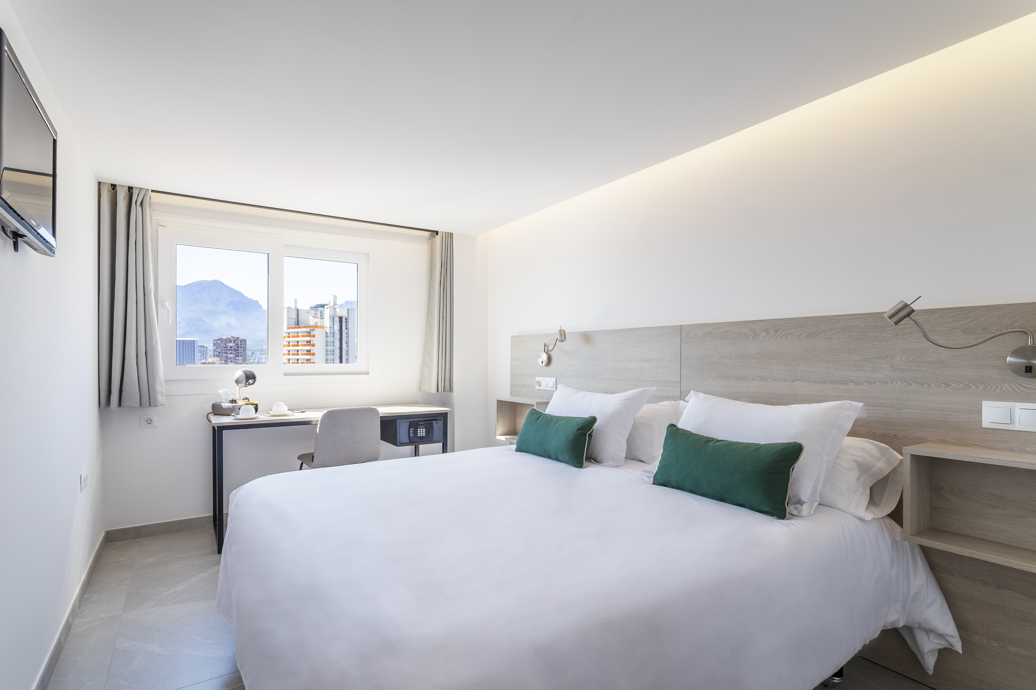 Bright modern hotel room with queen bed, desk, and mountain city view.