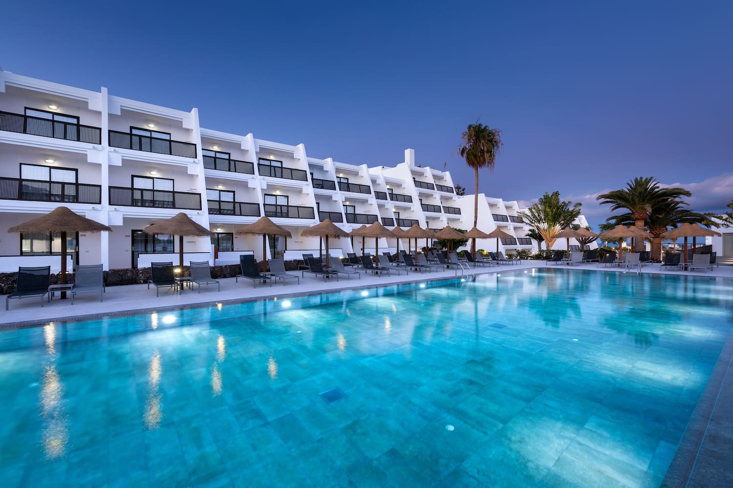 a pool with umbrellas and chairs in front of a hotel