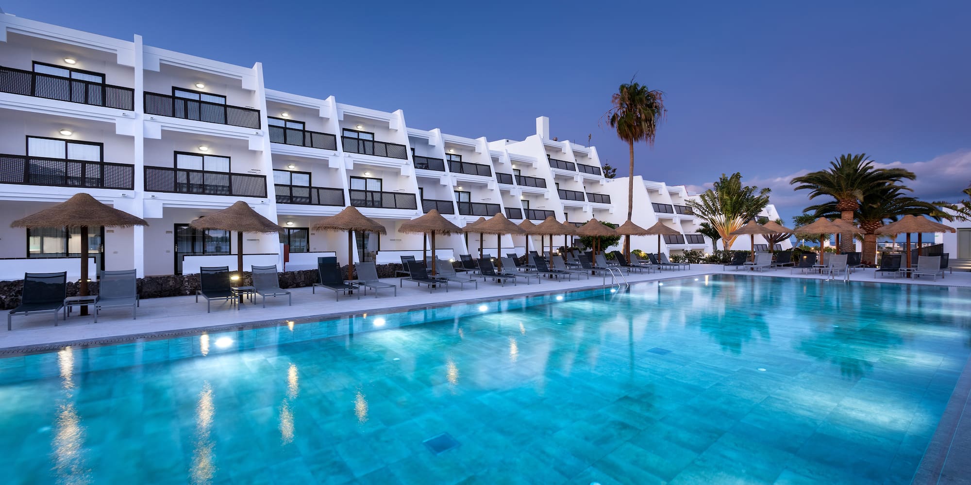 a pool with umbrellas and chairs in front of a hotel
