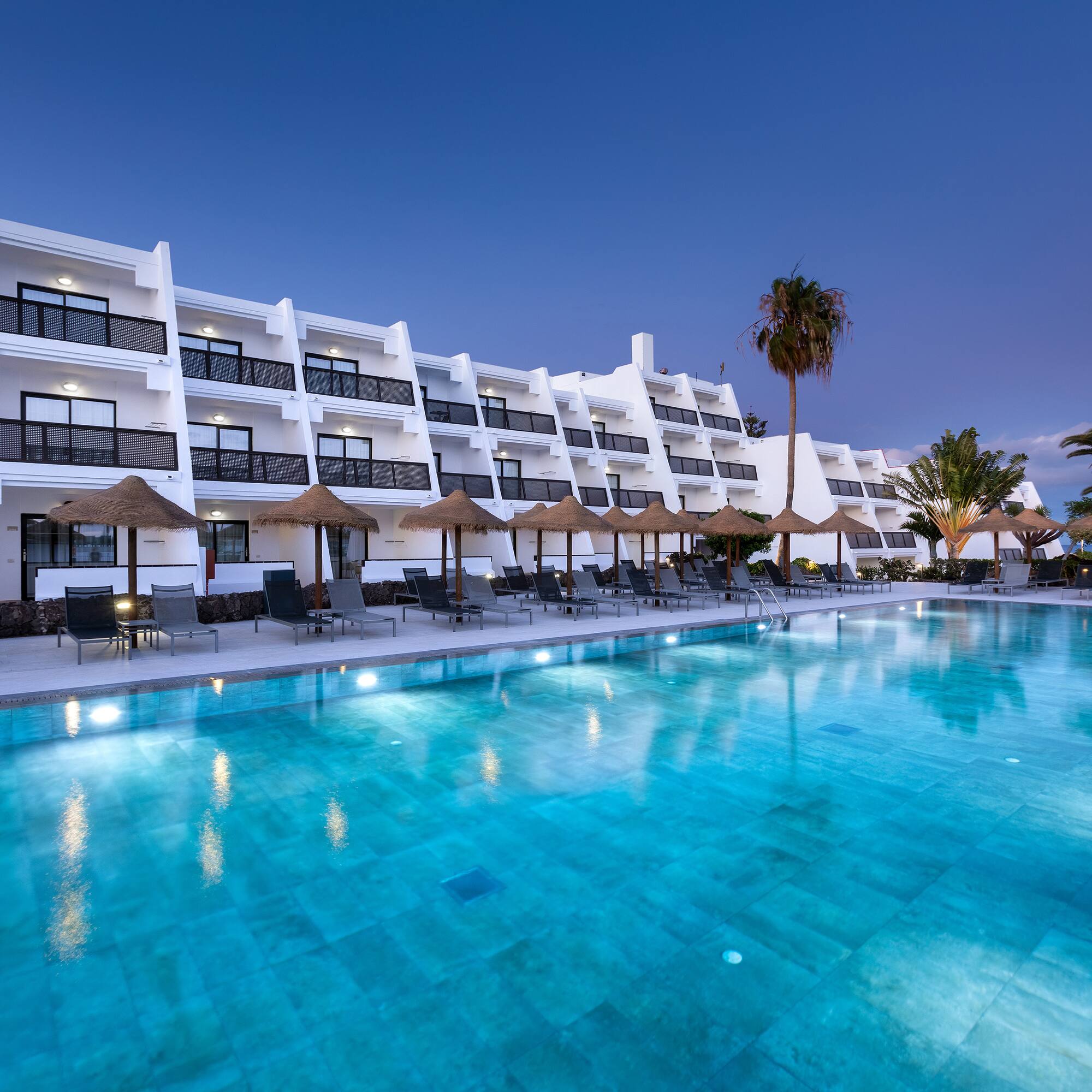 a pool with umbrellas and chairs in front of a hotel