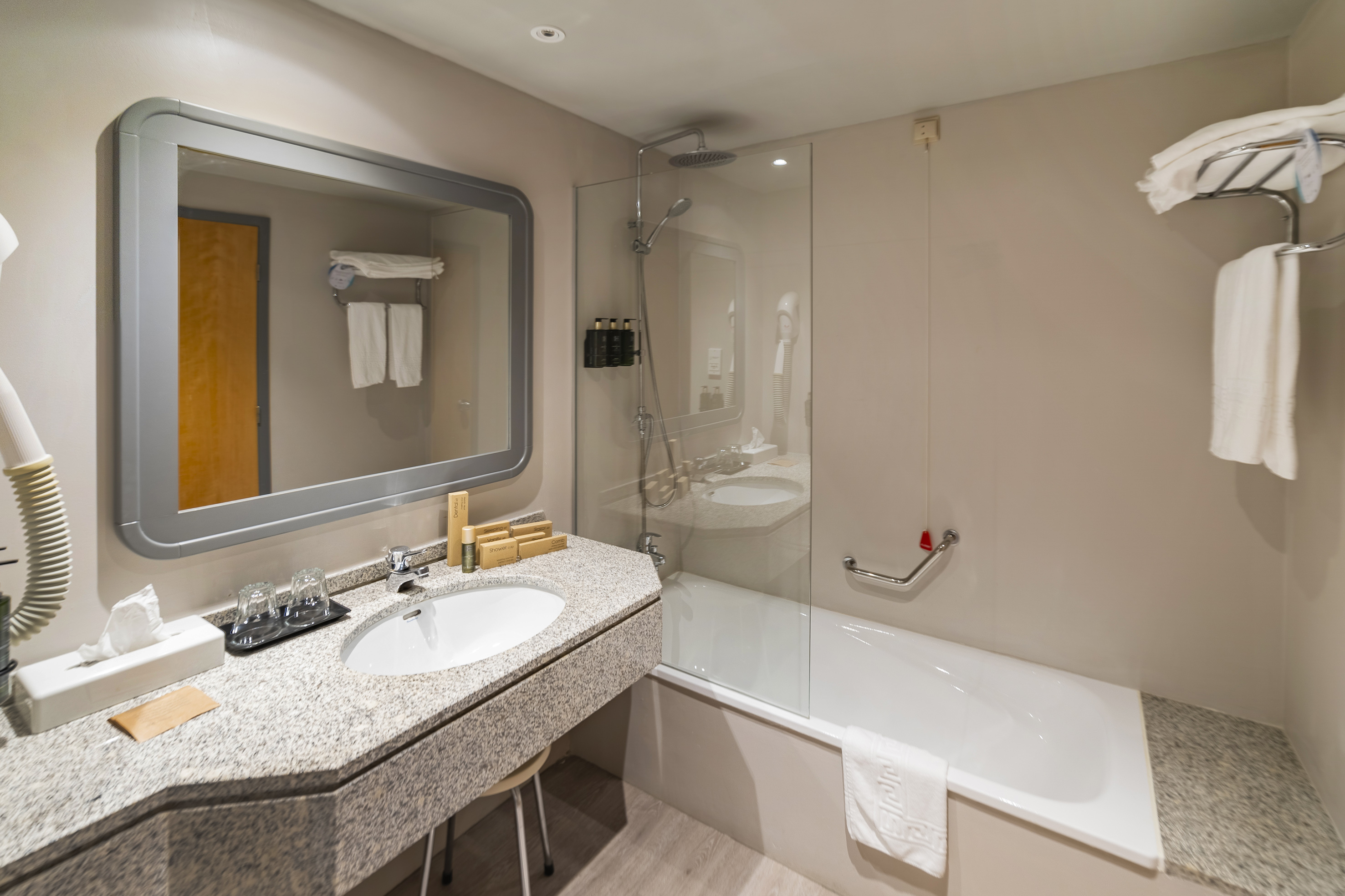 Modern hotel bathroom featuring granite vanity, sink, mirror, and shower-bathtub.