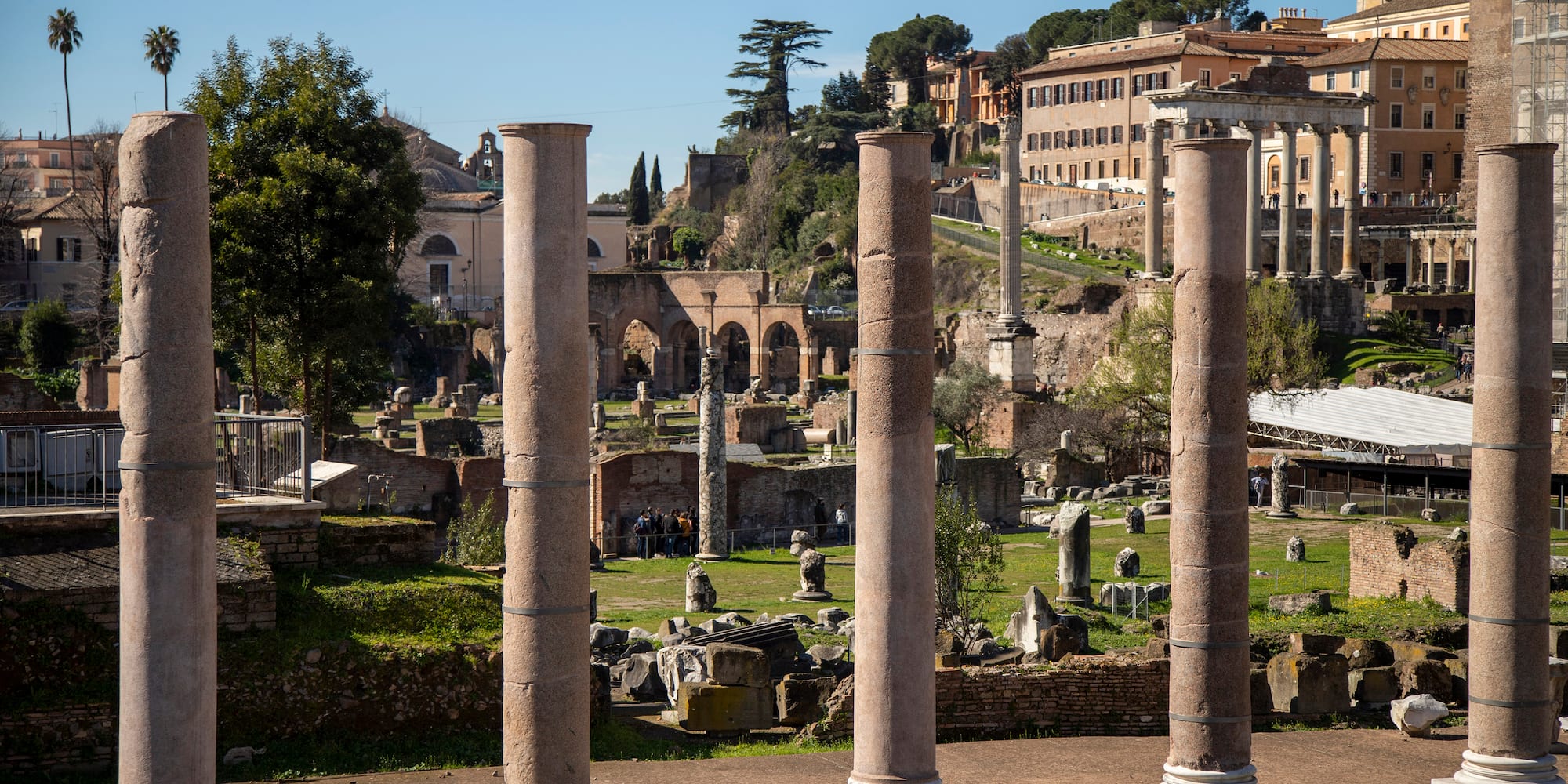 a group of pillars in a grassy area with buildings in the background