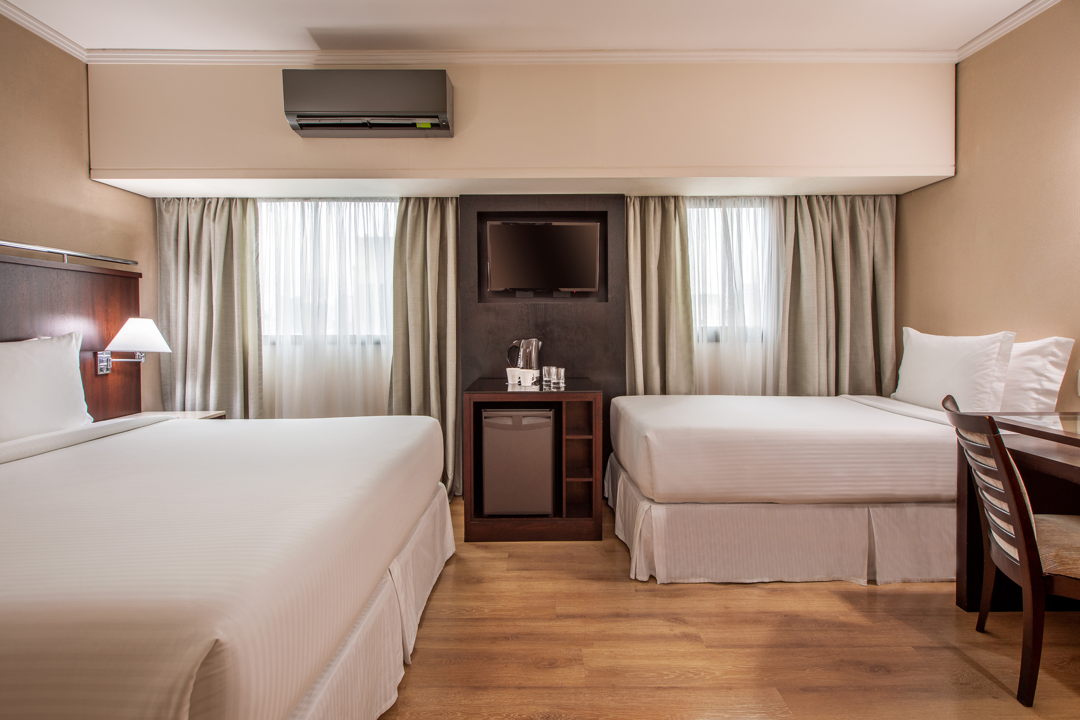 Hotel guest room with two beds, wall TV, mini-fridge, and AC unit.