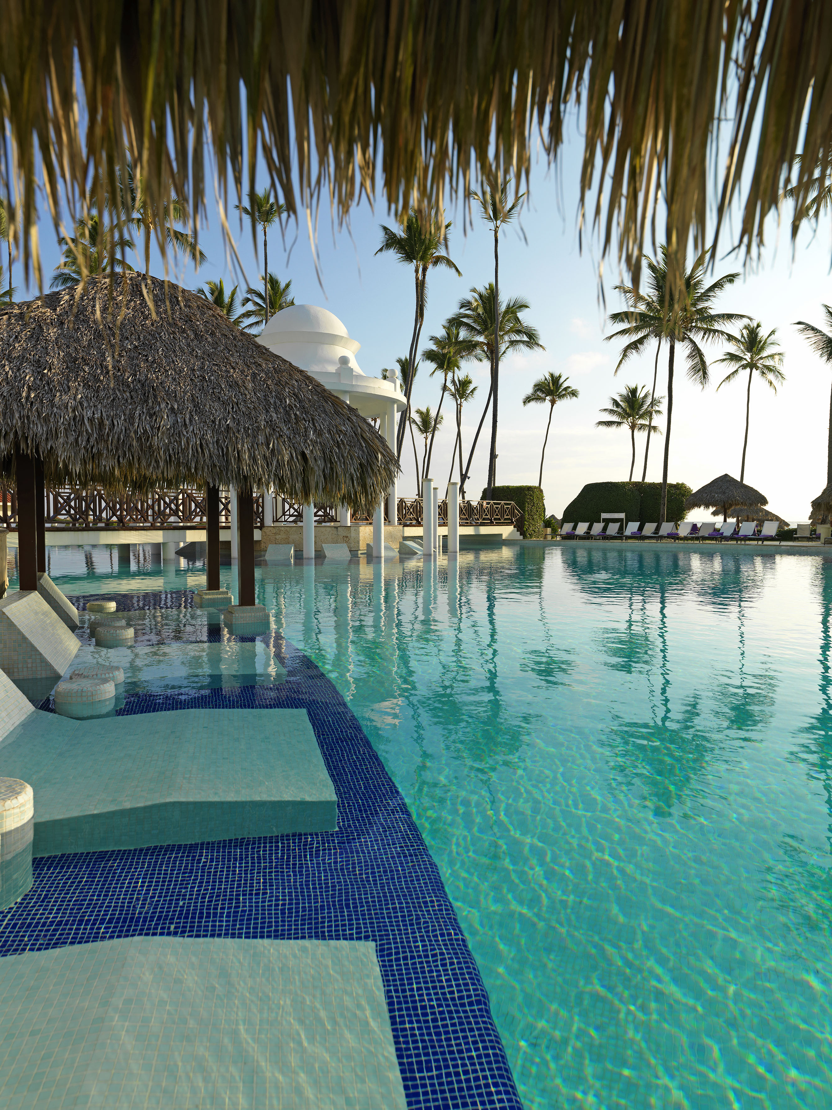 Luxury resort pool with swim-up bar, thatched cabana, gazebo, and palm trees.
