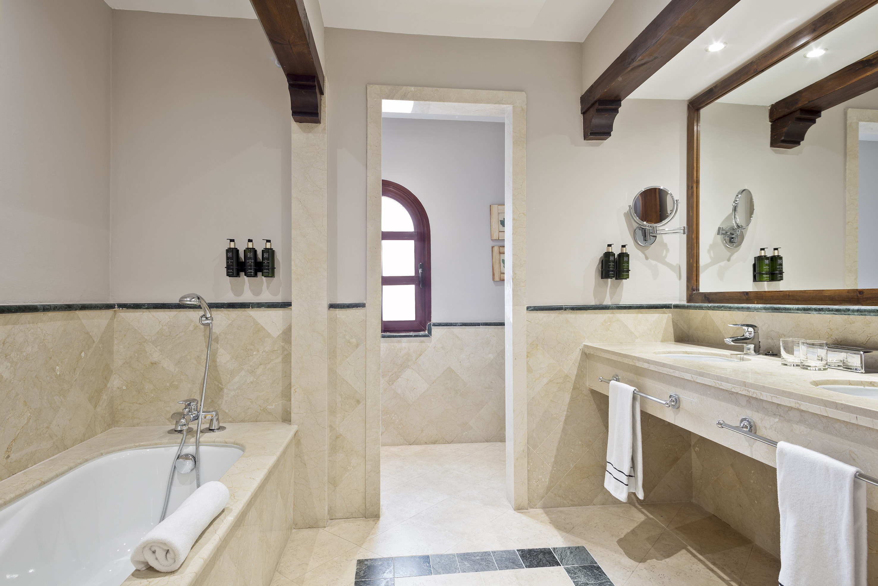 Elegant marble bathroom with bathtub, double vanity, and wooden ceiling beams.