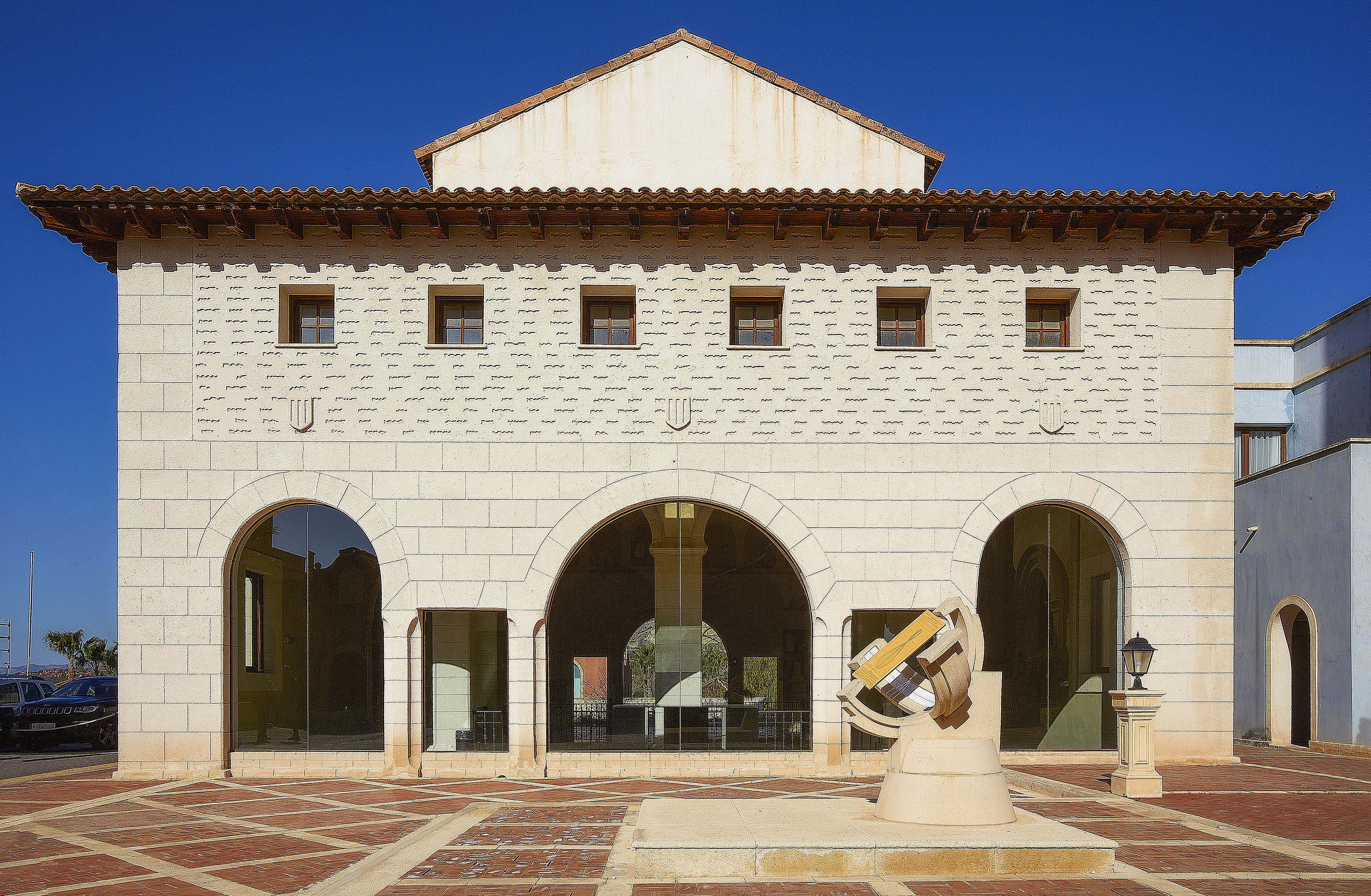 Stone building with arches, tiled roof, and an armillary sphere in courtyard.