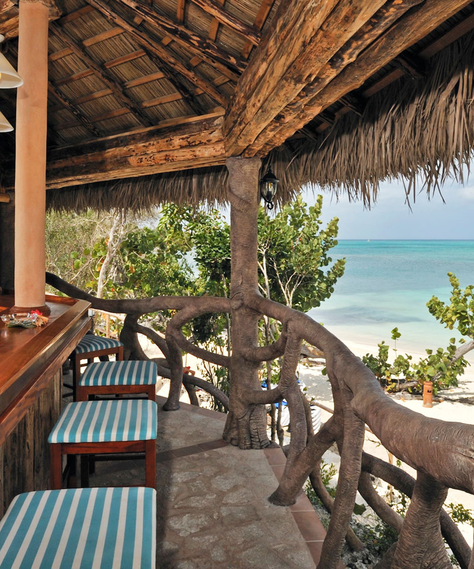 a bar with chairs and a thatched roof overlooking the ocean