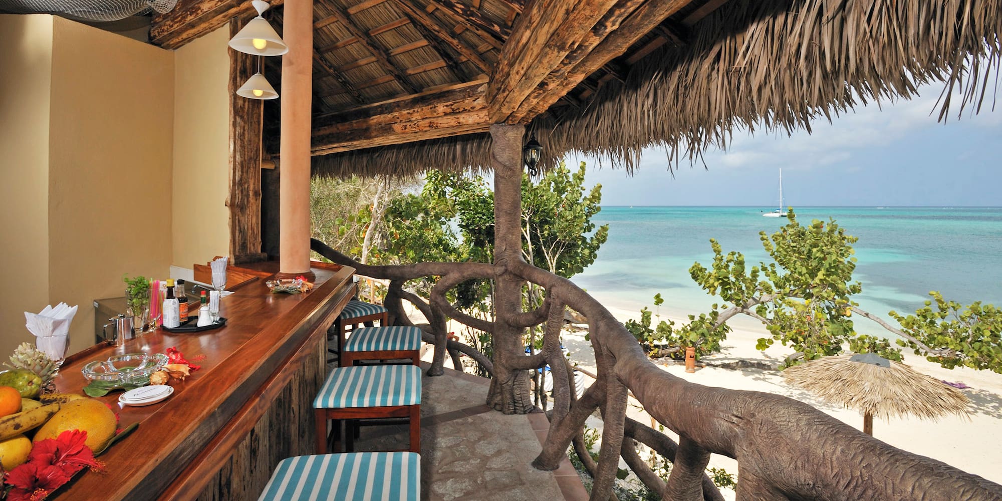 a bar with chairs and a thatched roof overlooking the ocean