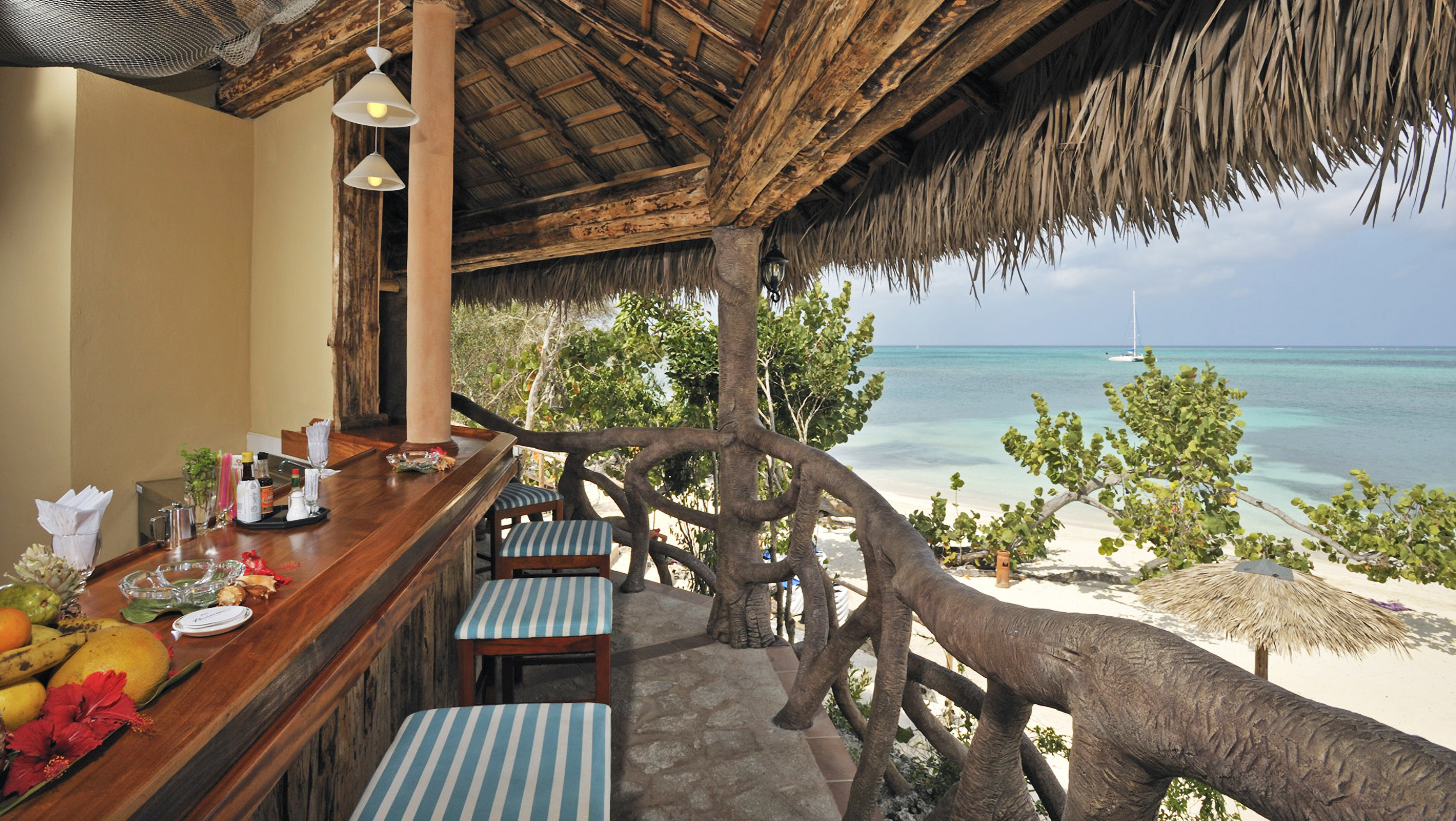 a bar with chairs and a thatched roof overlooking the ocean