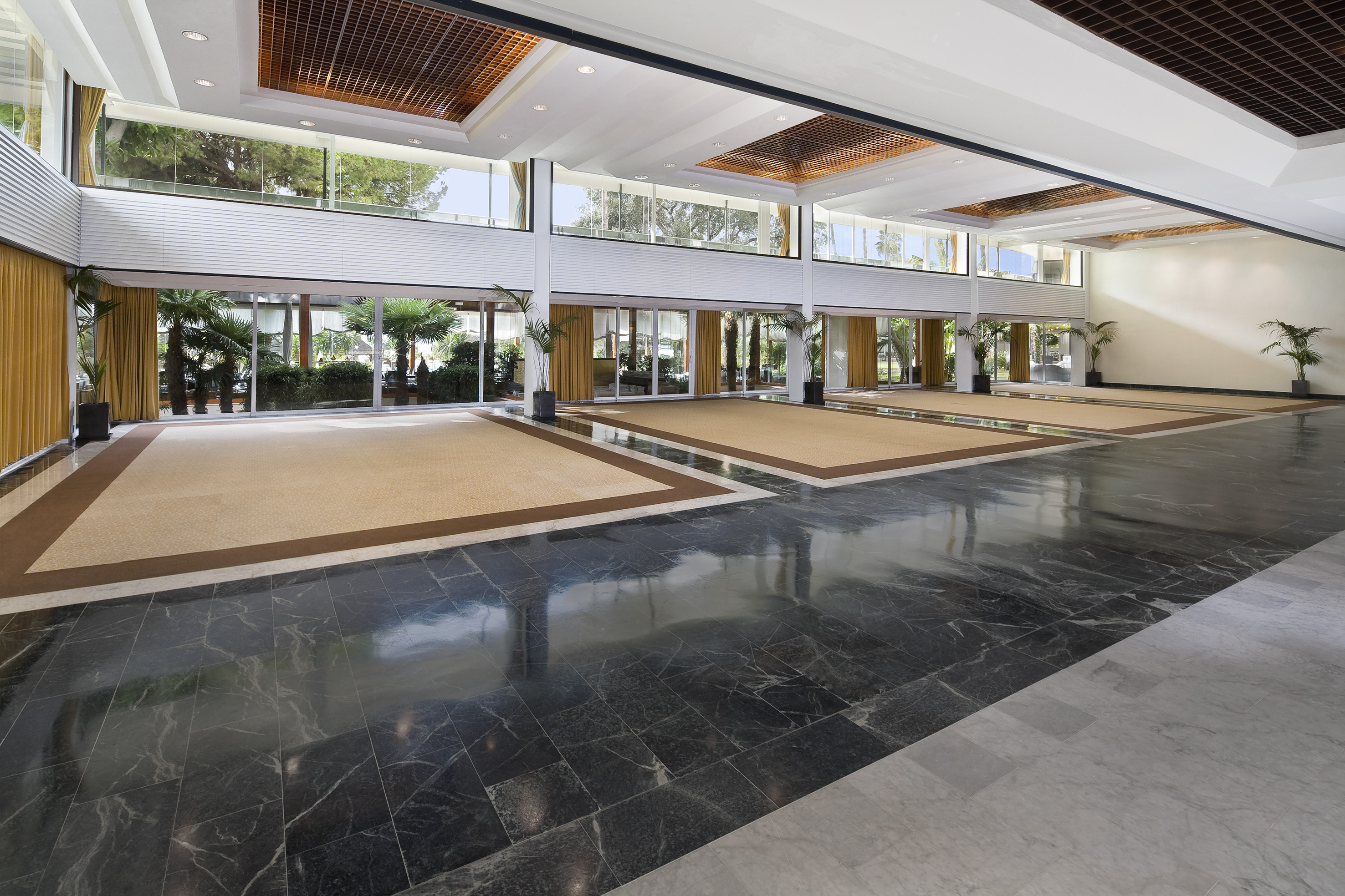 Spacious hotel lobby with dark marble floors, large windows, and beige carpet areas.