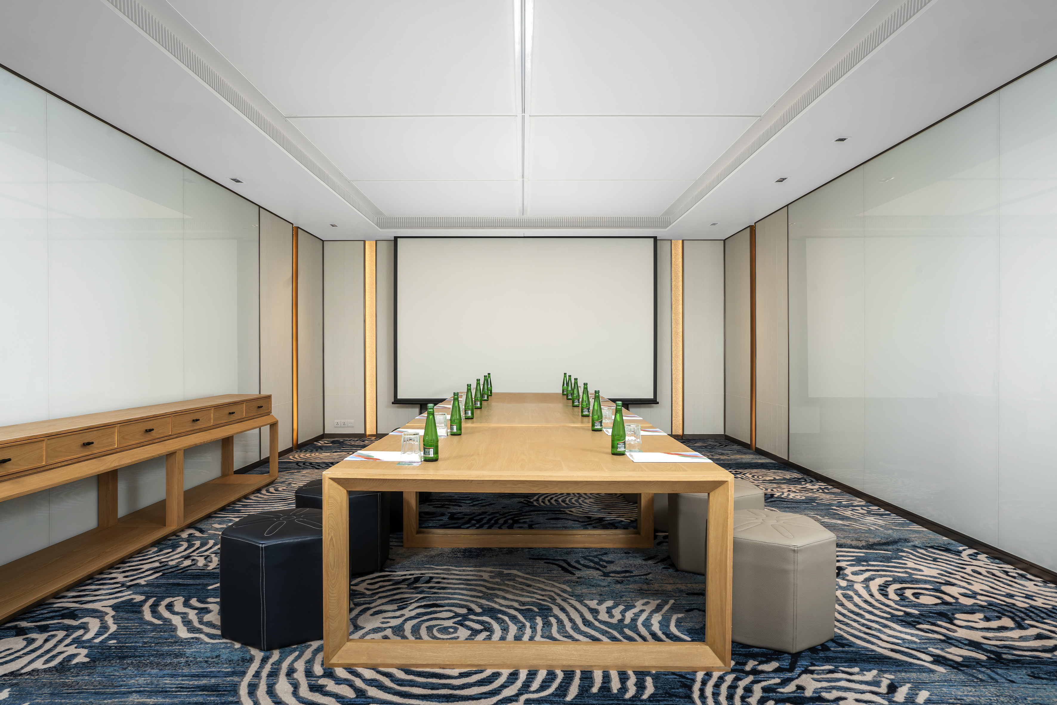 Modern conference room with long wooden table, screen, and patterned carpet.