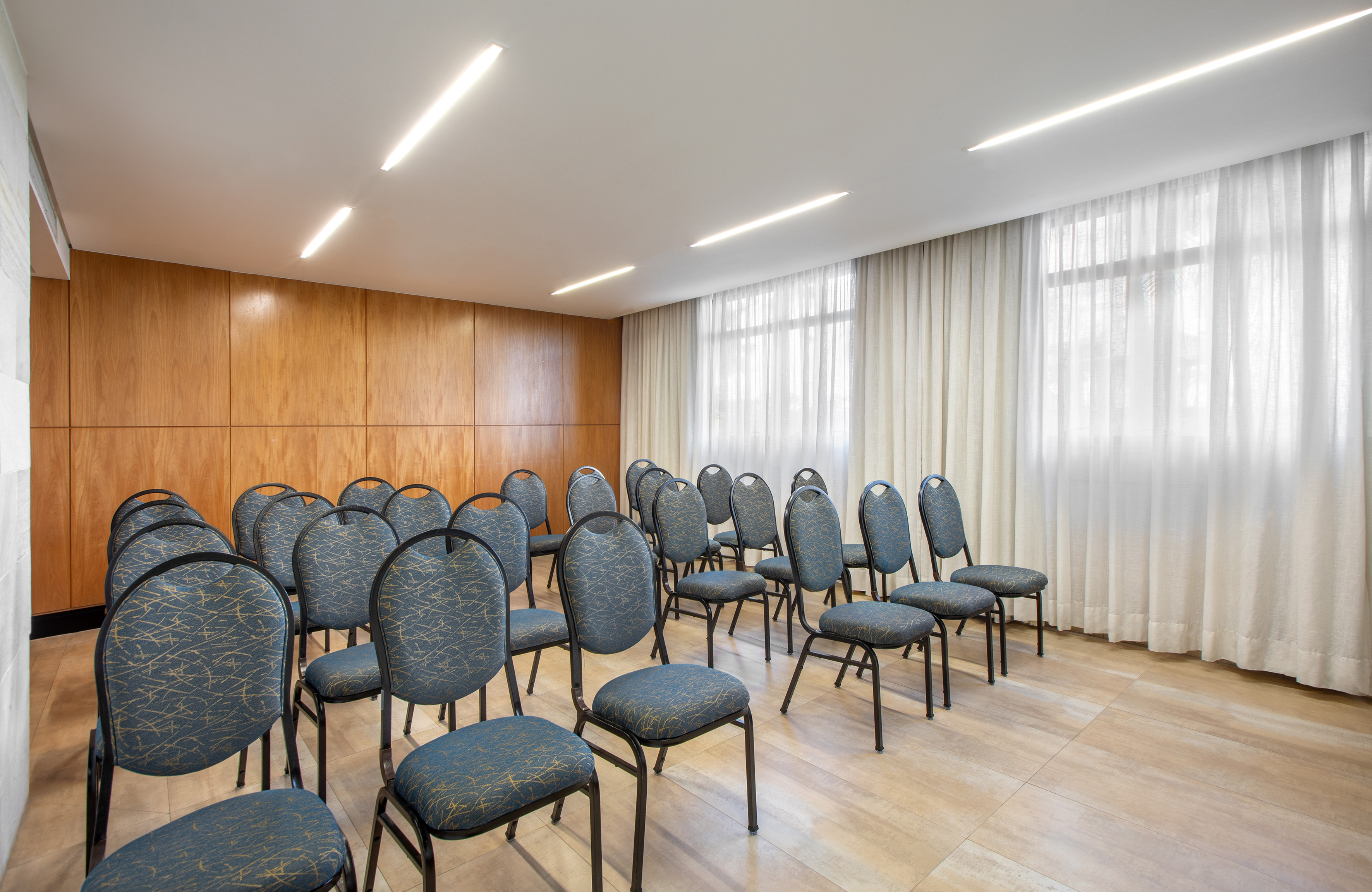 Empty conference room setup with blue chairs, wood paneling, and white curtains.