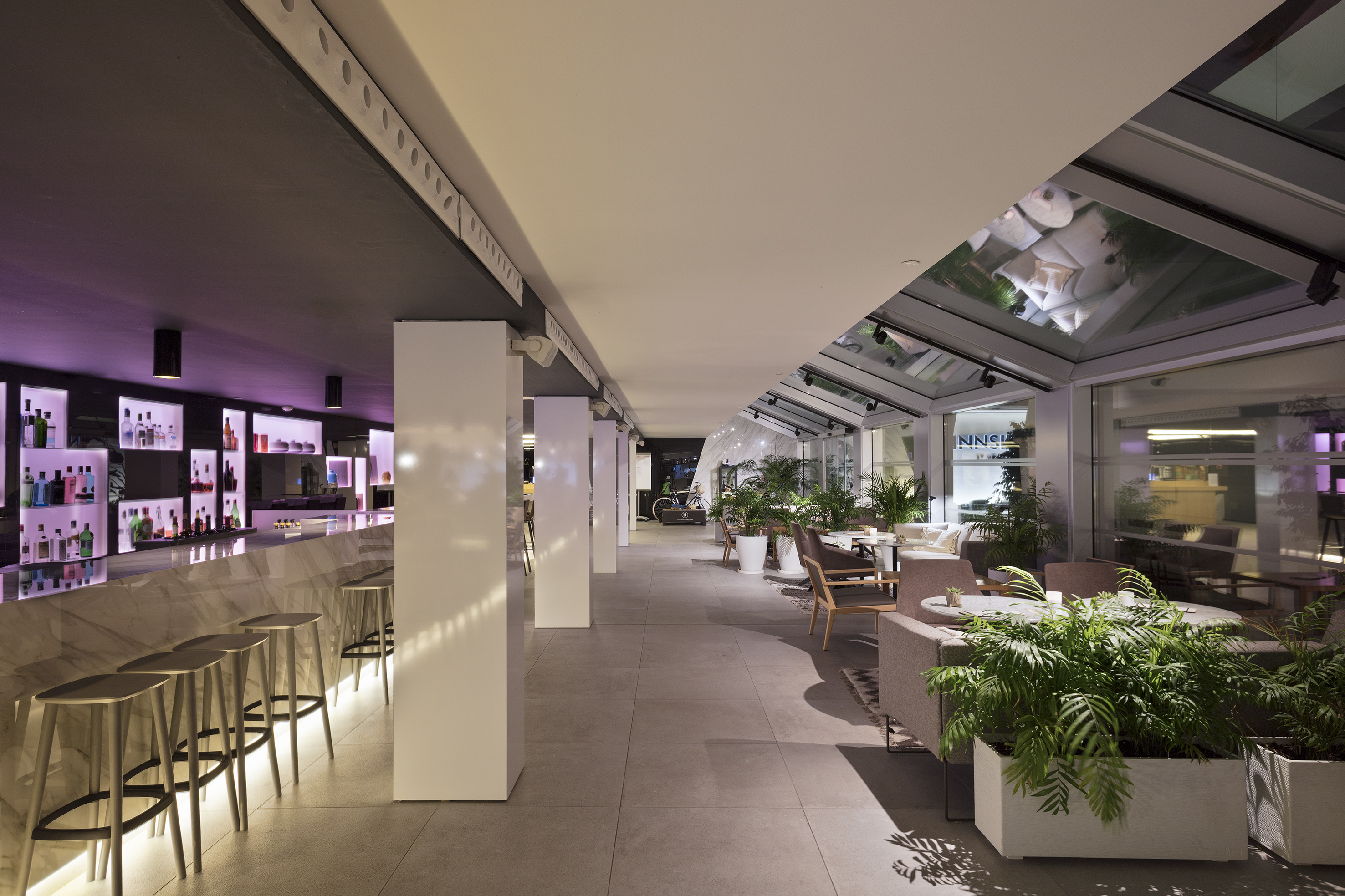 Stylish hotel bar with glowing counter, lounge seating, and indoor plants.