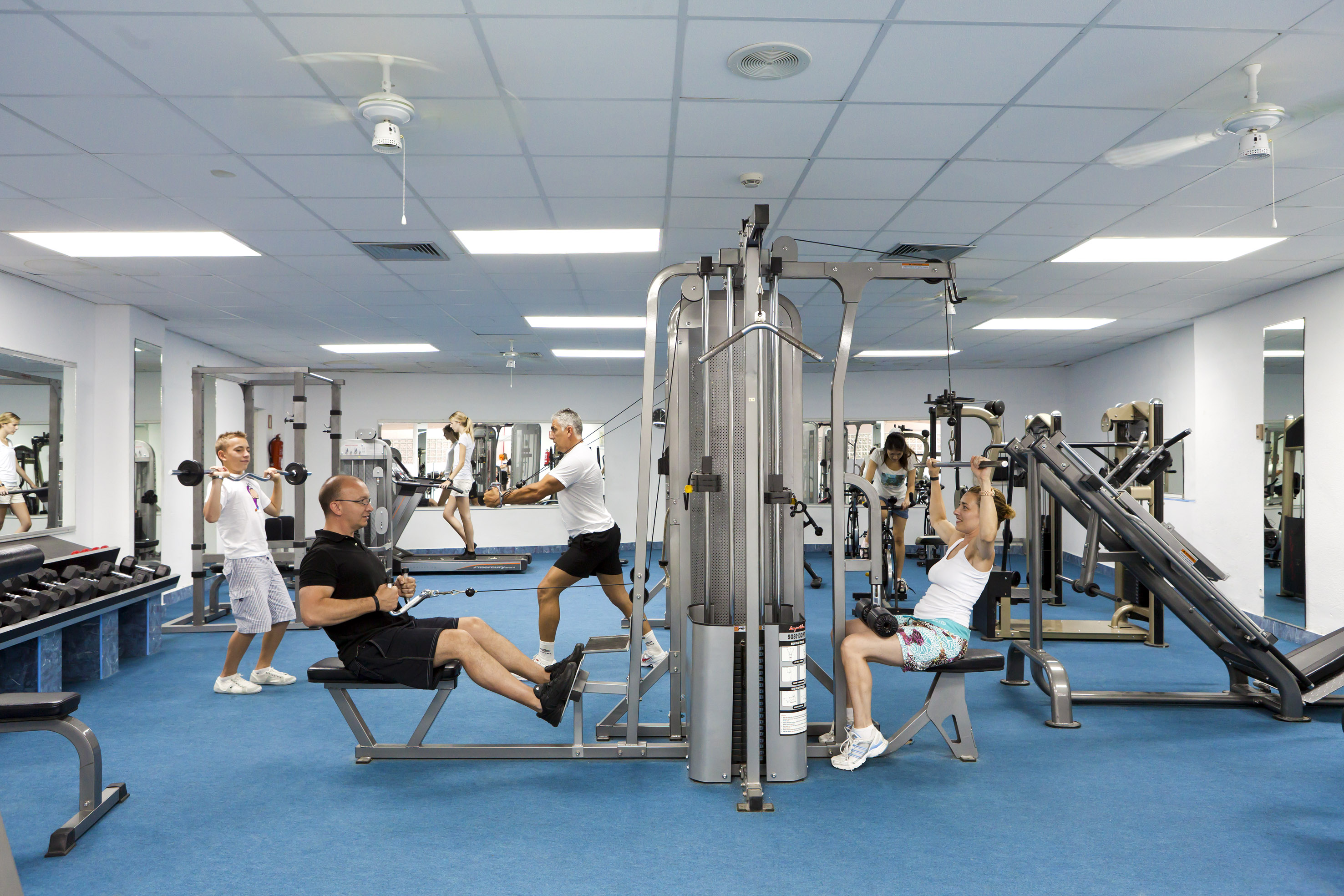 People exercising in a bright gym with weight machines and free weights. - SOL Lanzarote All Inclusive, Lanzarote