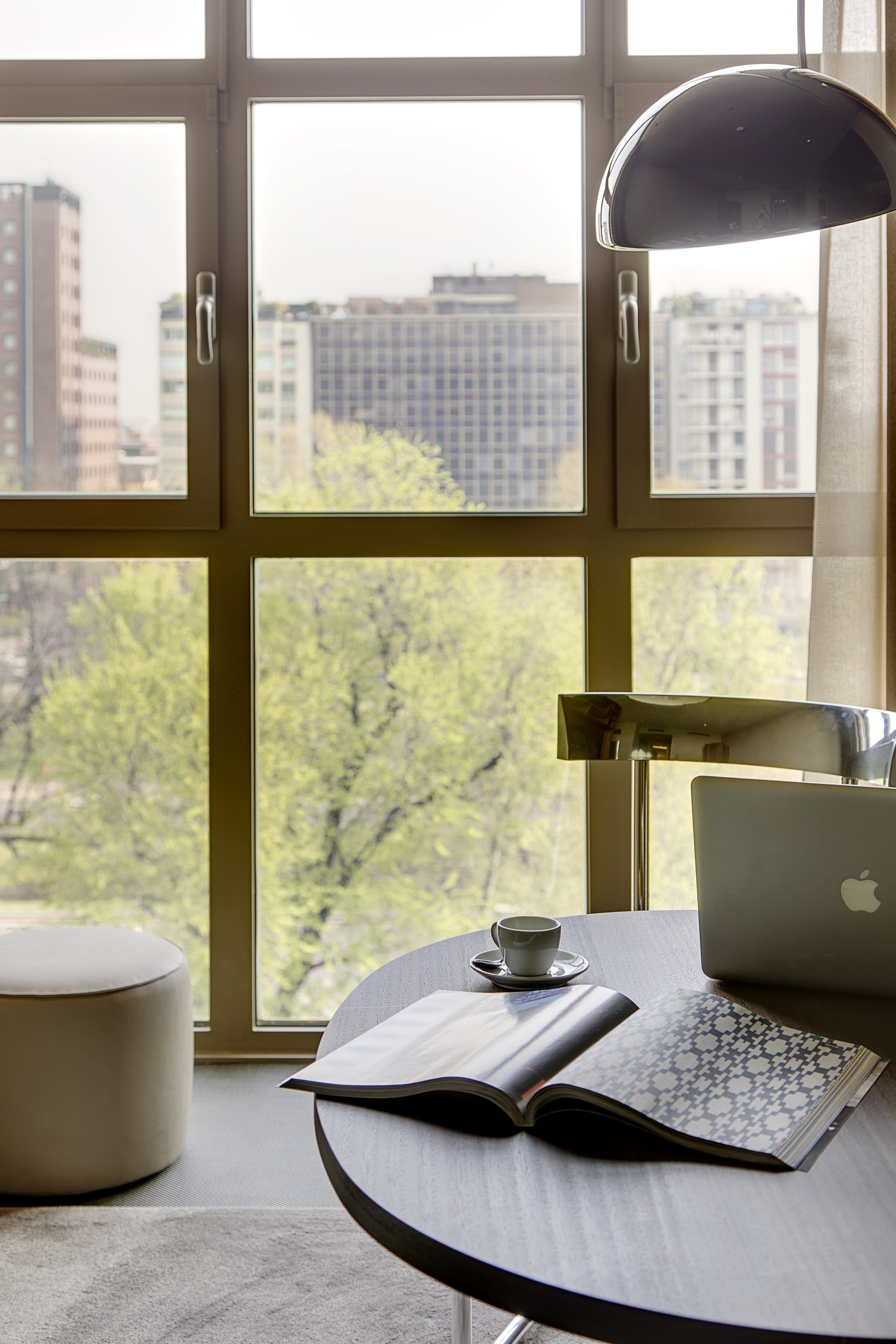 Modern workspace by window with laptop, coffee, magazine, city view.