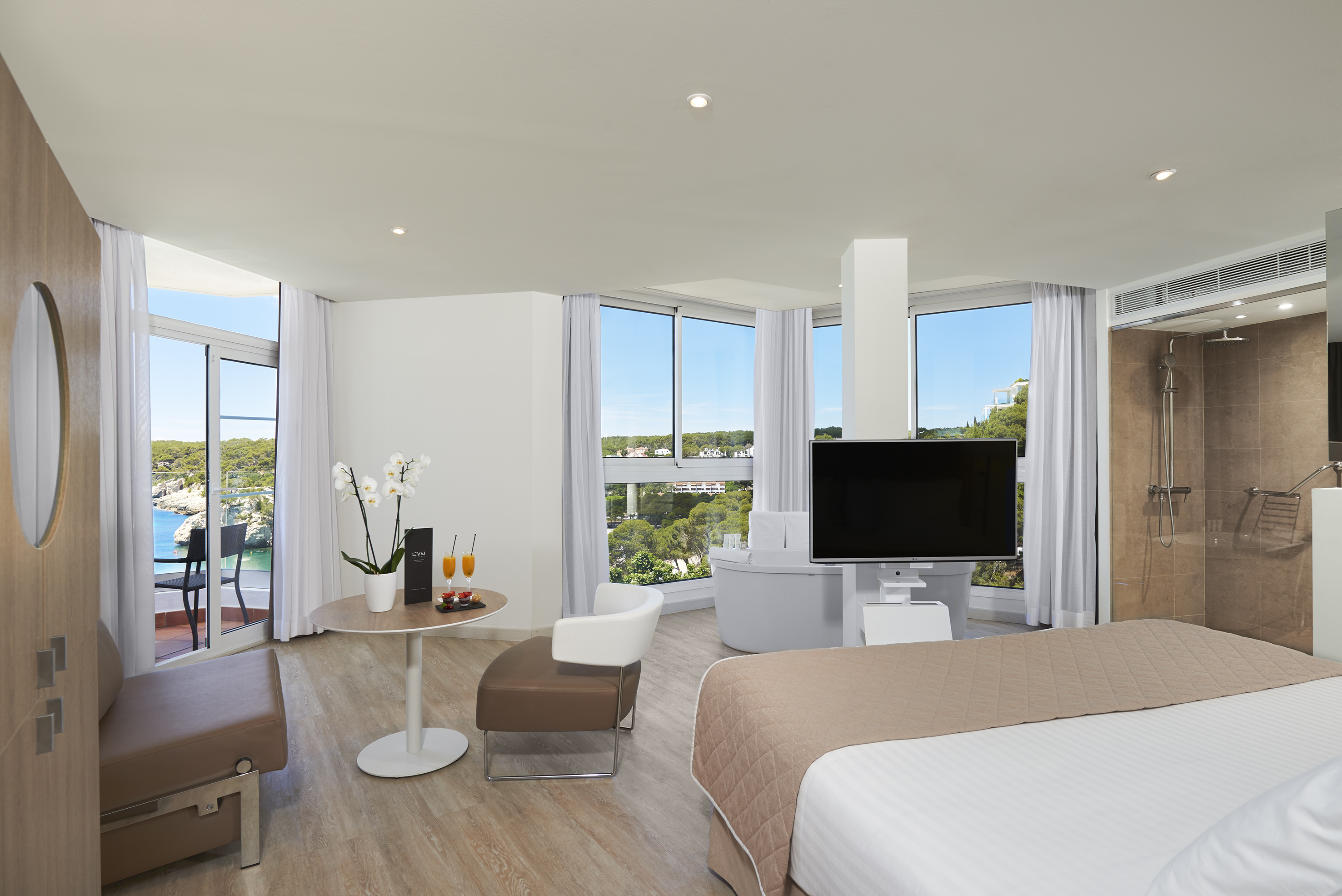 Modern hotel suite with sea view balcony, luxurious bed, flat-screen TV, and lounge.