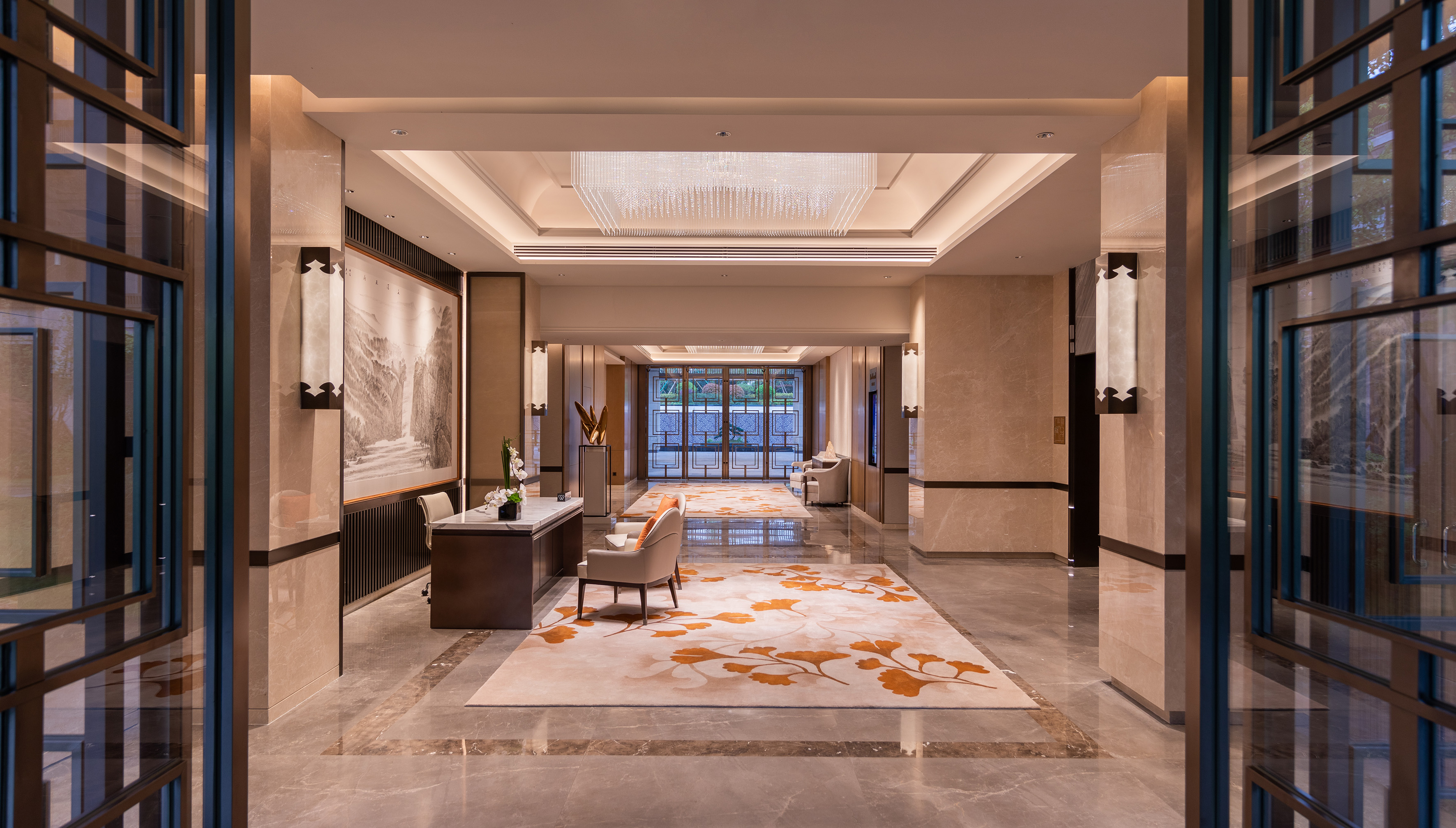 Elegant hotel lobby with chandelier, reception, marble, and ginkgo-patterned rug.