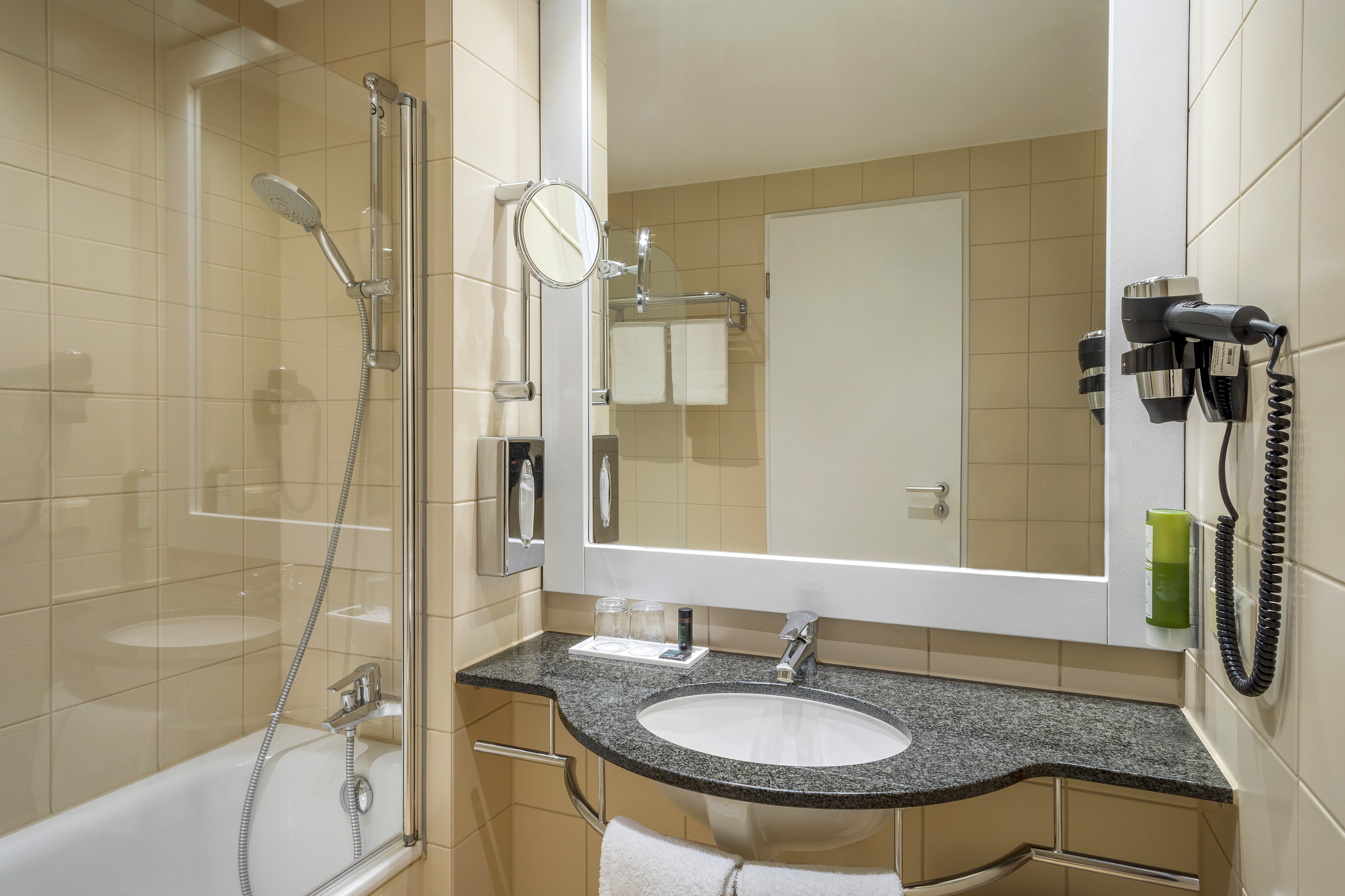 Clean hotel bathroom with bathtub, shower, modern vanity sink, mirror, and hairdryer.