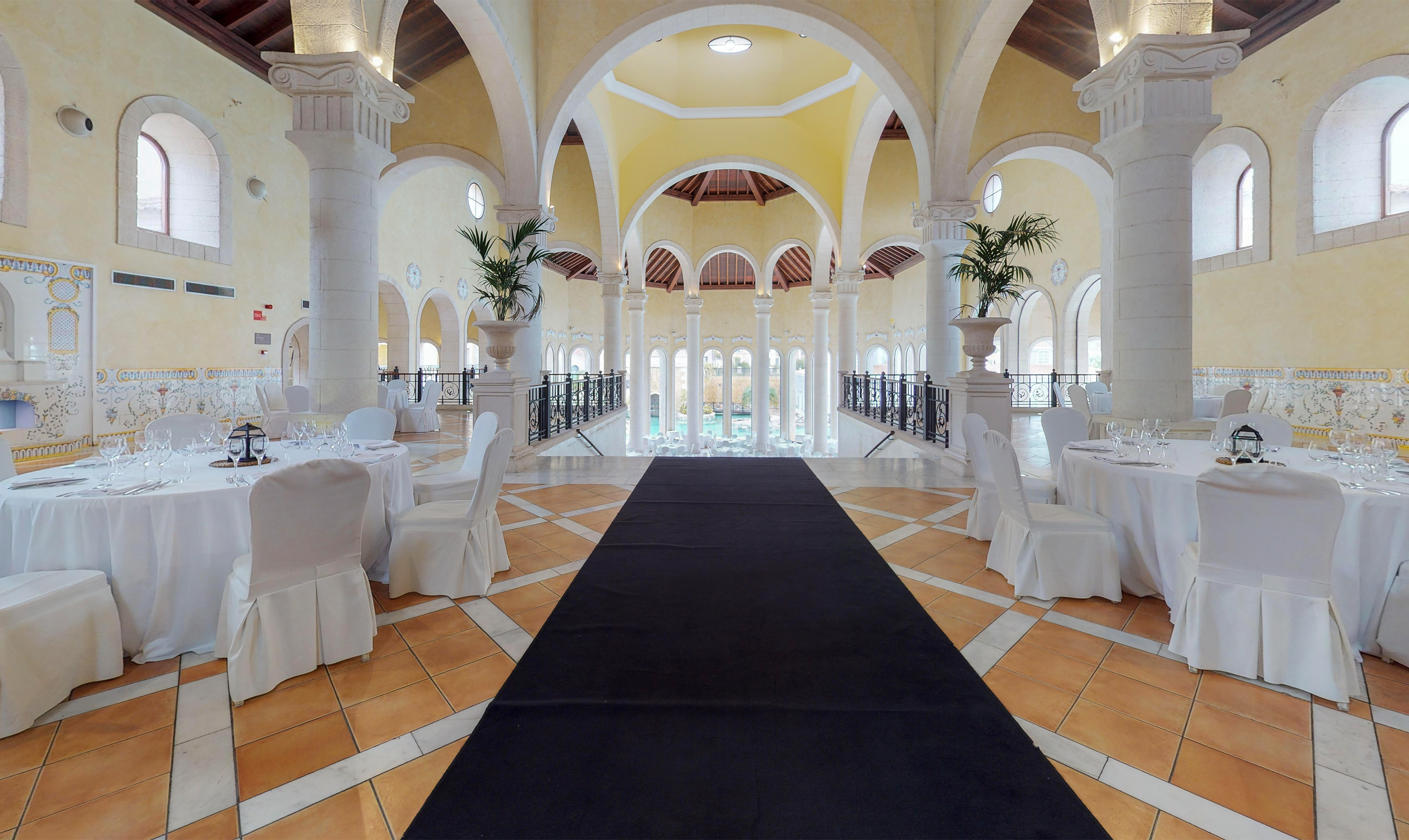 Elegant reception hall with classical arches, set tables, and central walkway.