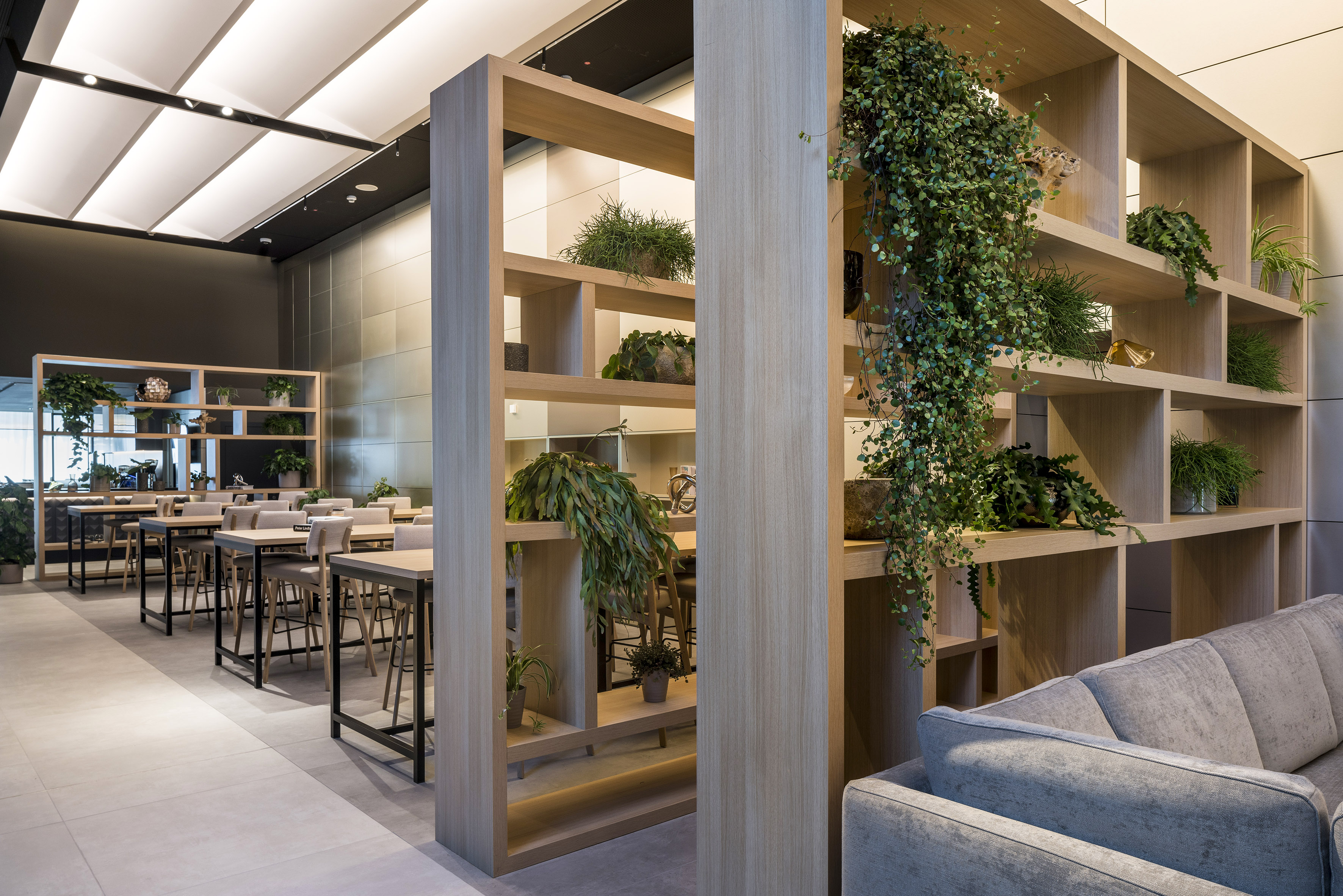 a room with a tall shelf with plants and tables
