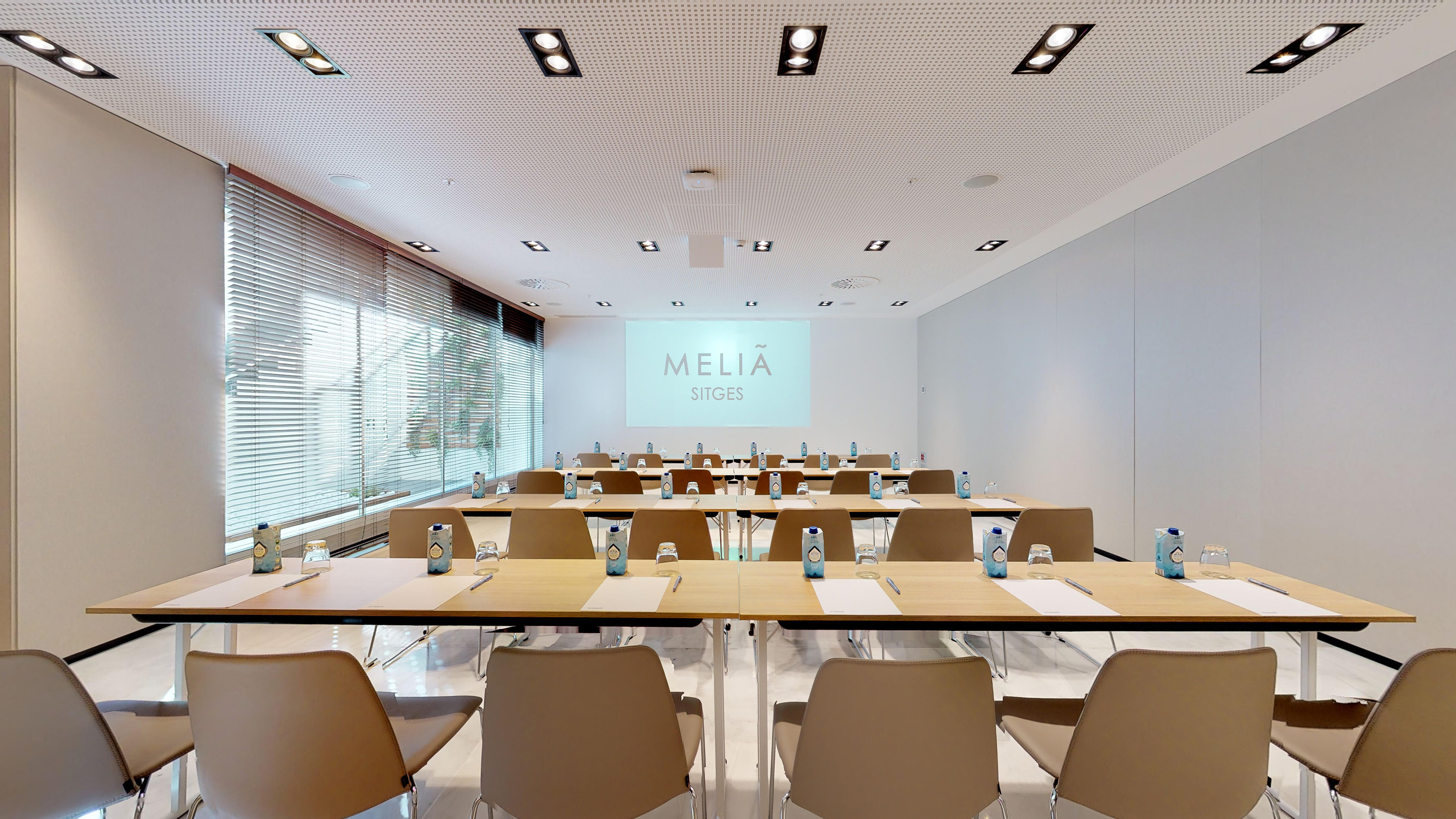 Modern Meliá Sitges conference room with classroom setup and projector screen.