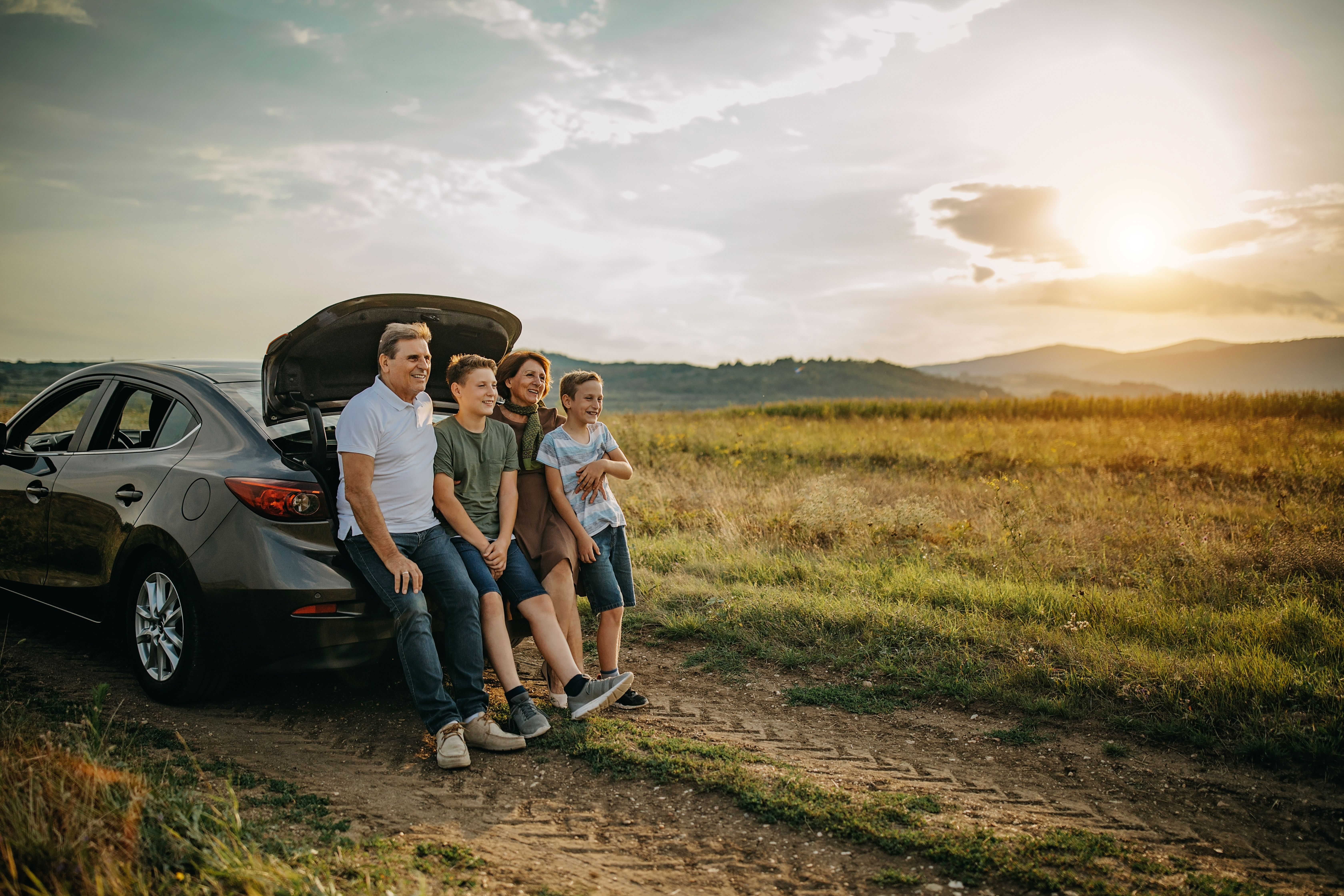 Familia sonriendo en el maletero del coche al atardecer, viaje familiar.