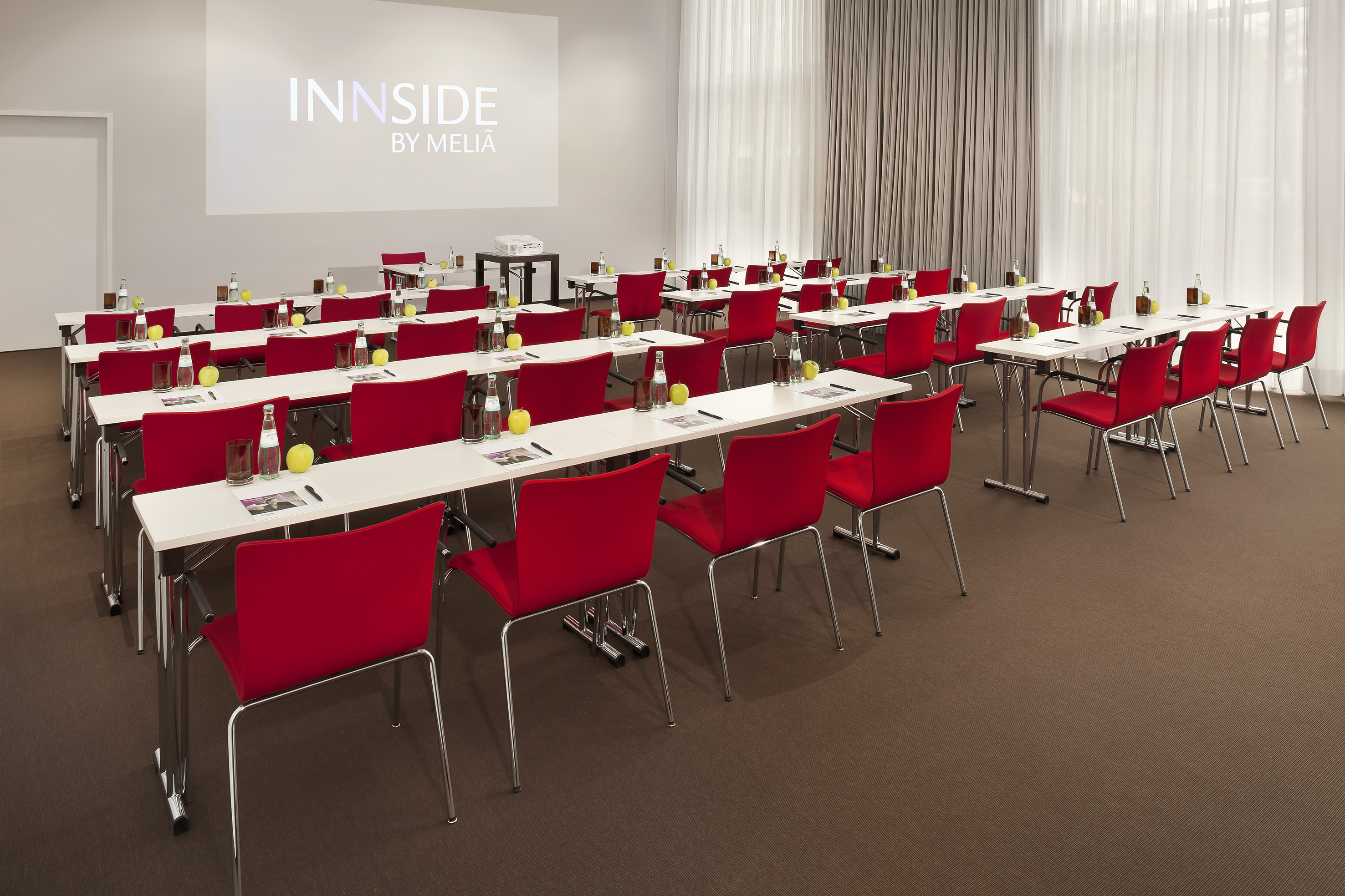 Innside by Meliá meeting room with red chairs, tables, and projector screen.