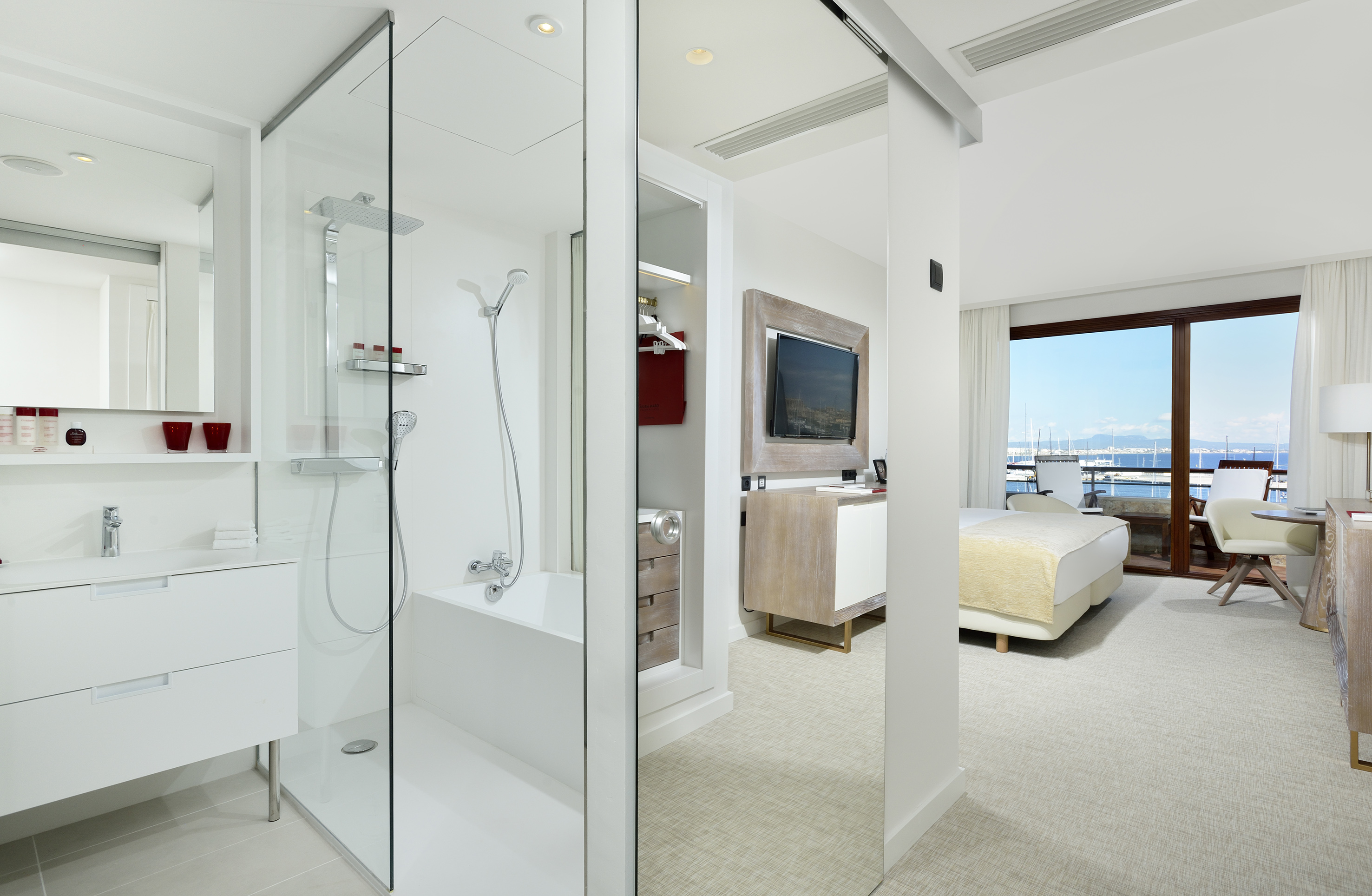 Modern hotel room with open bathroom, glass shower, and marina view.