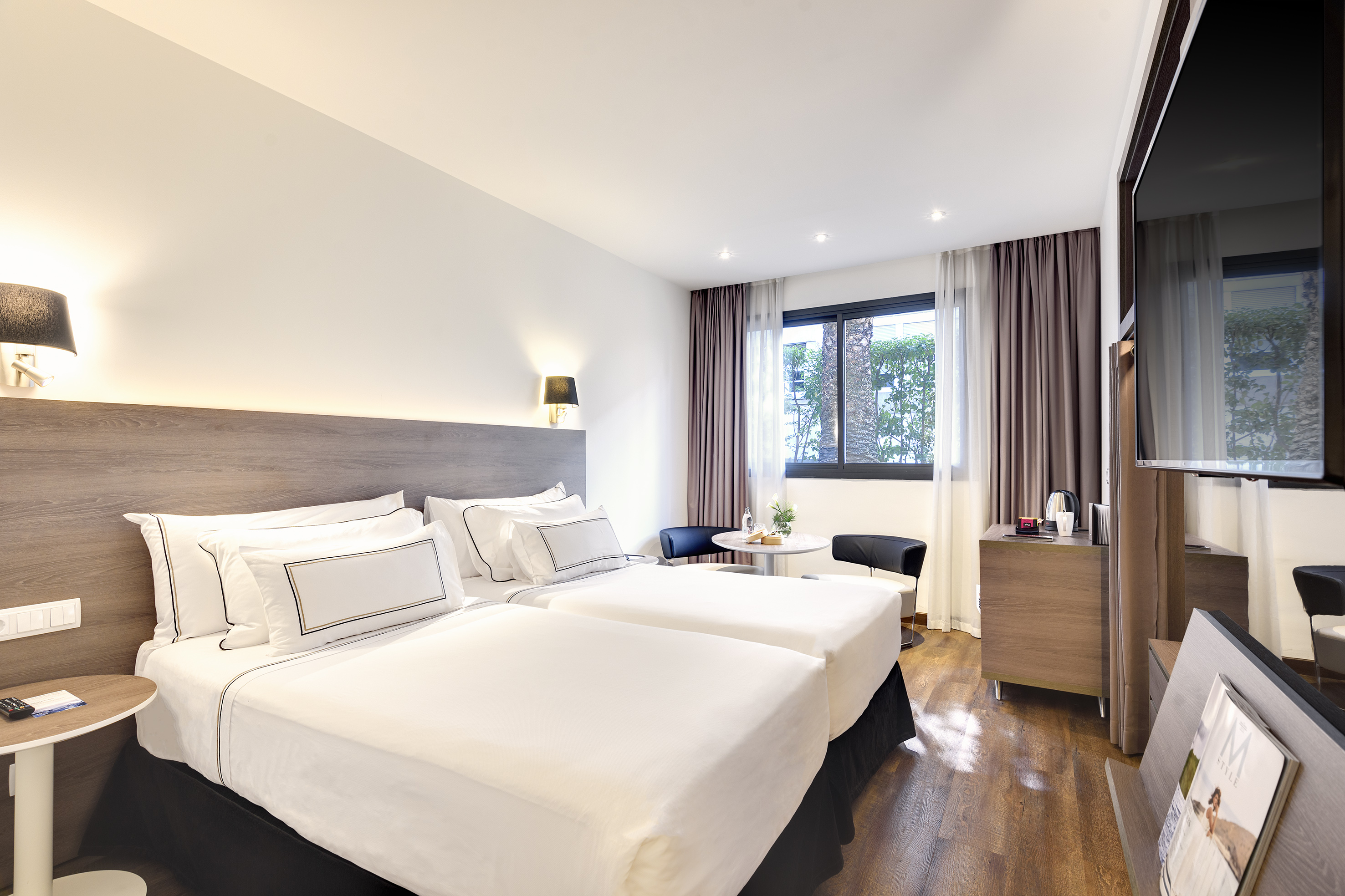 Modern hotel room with twin beds, crisp white linens, window, and TV.