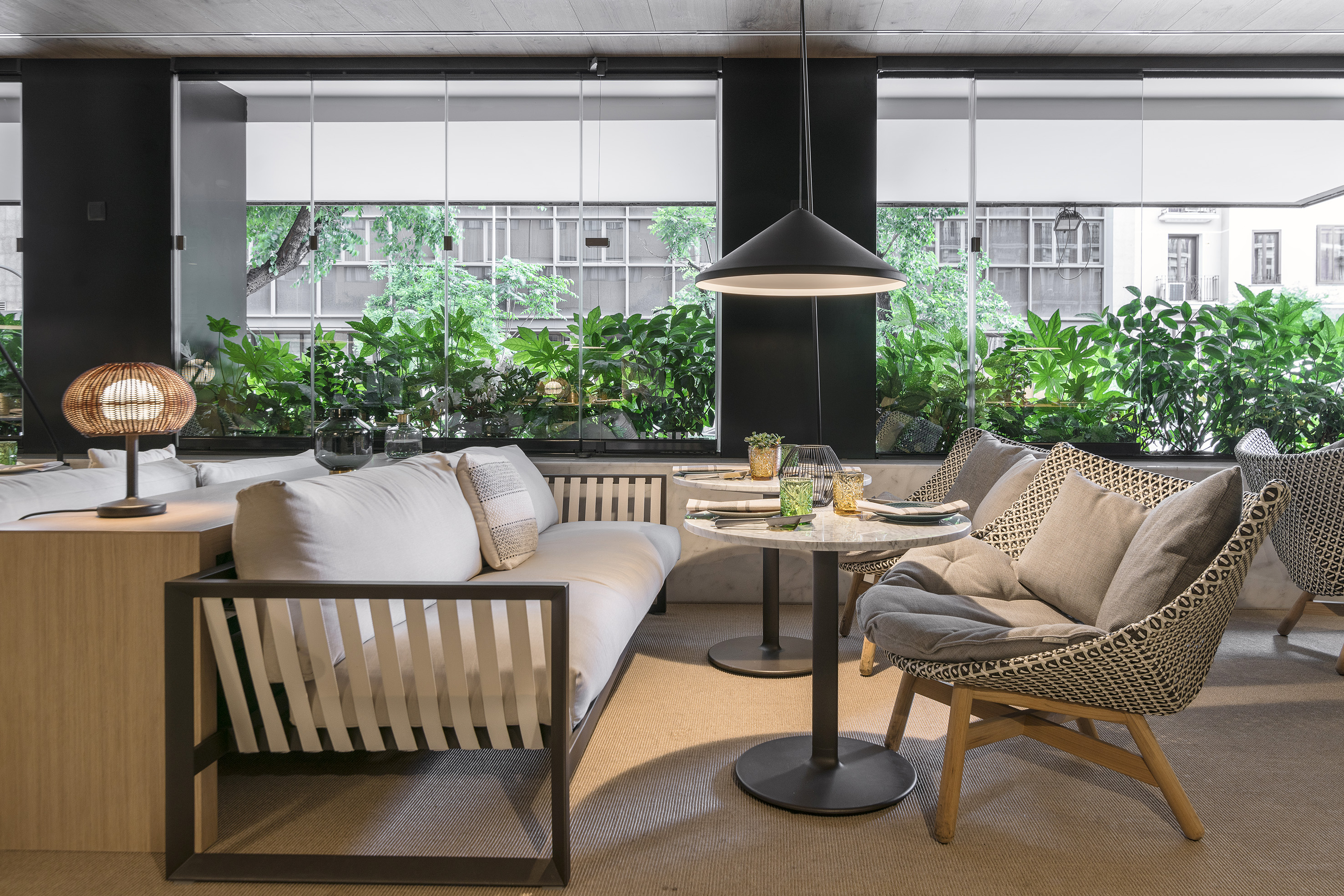 Modern cafe lounge with sofa, chairs, tables, and green window views.
