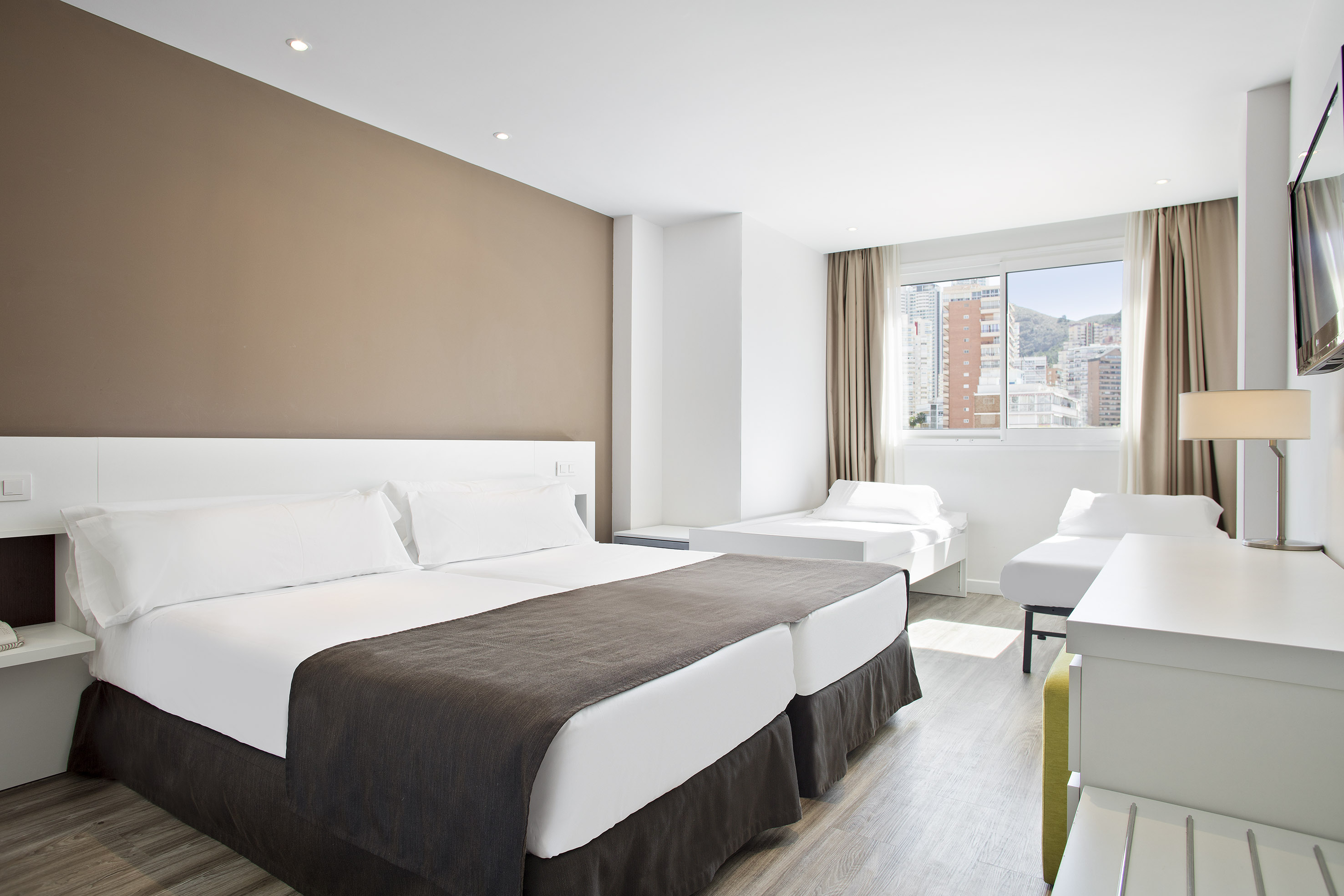 Modern hotel room with twin beds, two single beds, and city view.