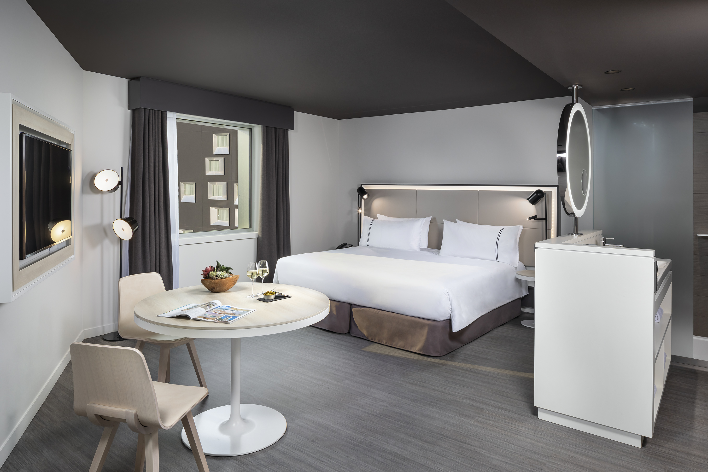 Modern hotel bedroom with king bed, dining table, and stylish vanity area.