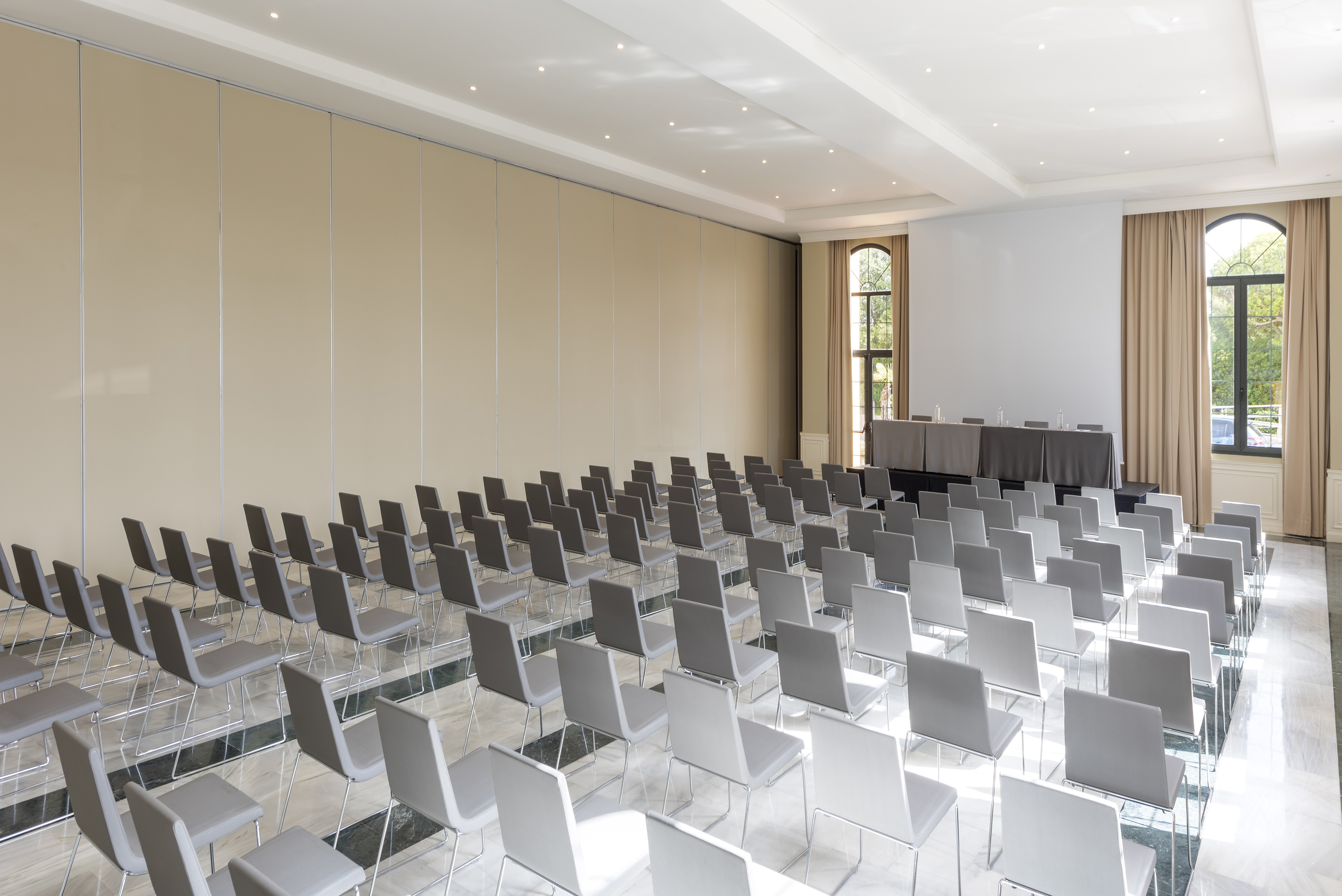Spacious conference room with theater seating, presentation table, and arch windows.