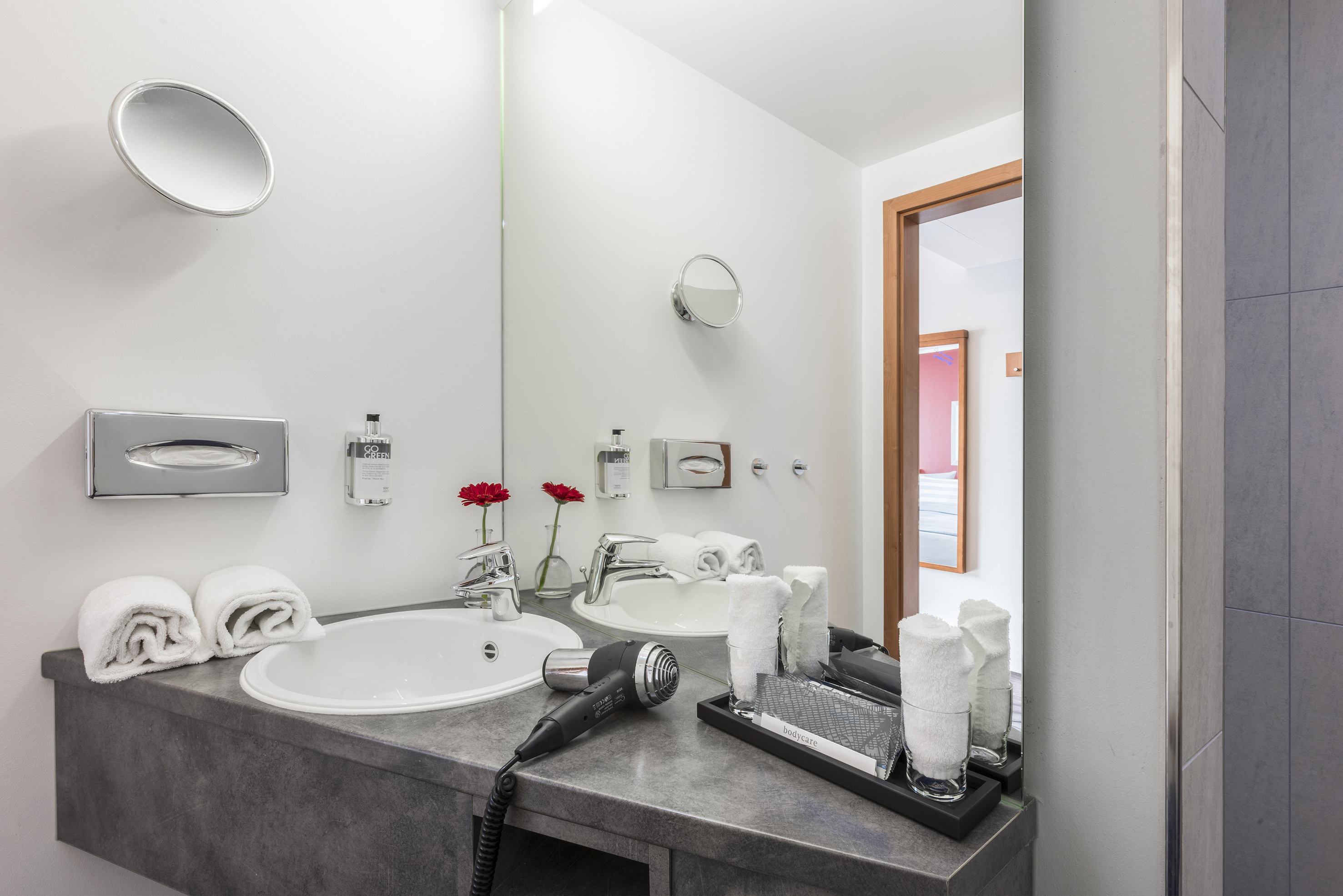 Modern hotel bathroom with double vanity, grey counter, white sinks, and towels.