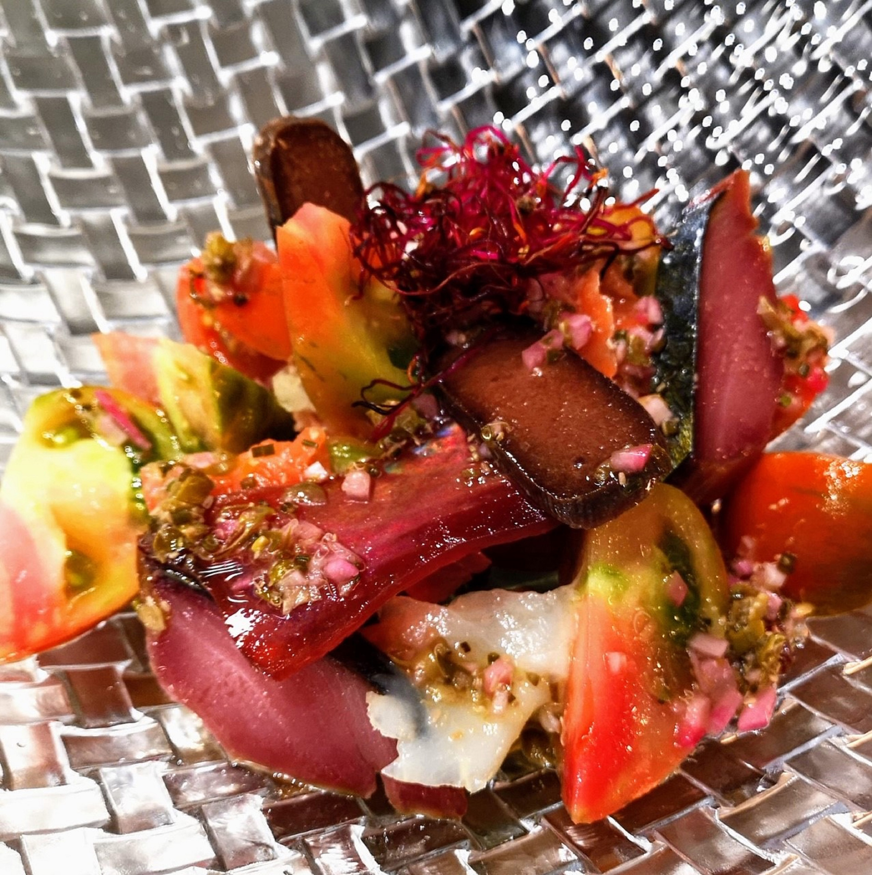 Heirloom tomato salad with dark fish slices and red microgreens.
