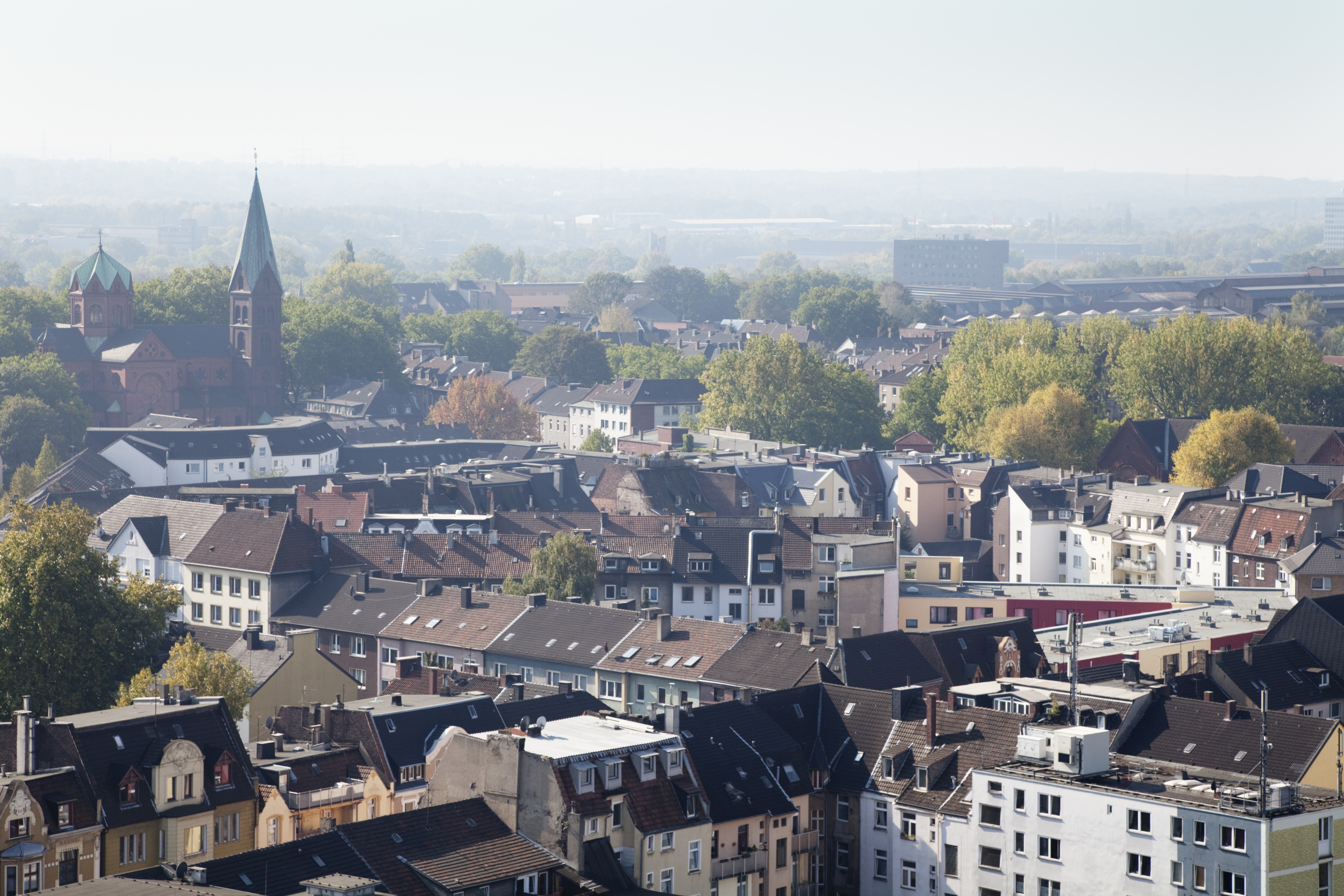 Urban panorama: red brick church, residential buildings, autumn trees, hazy.