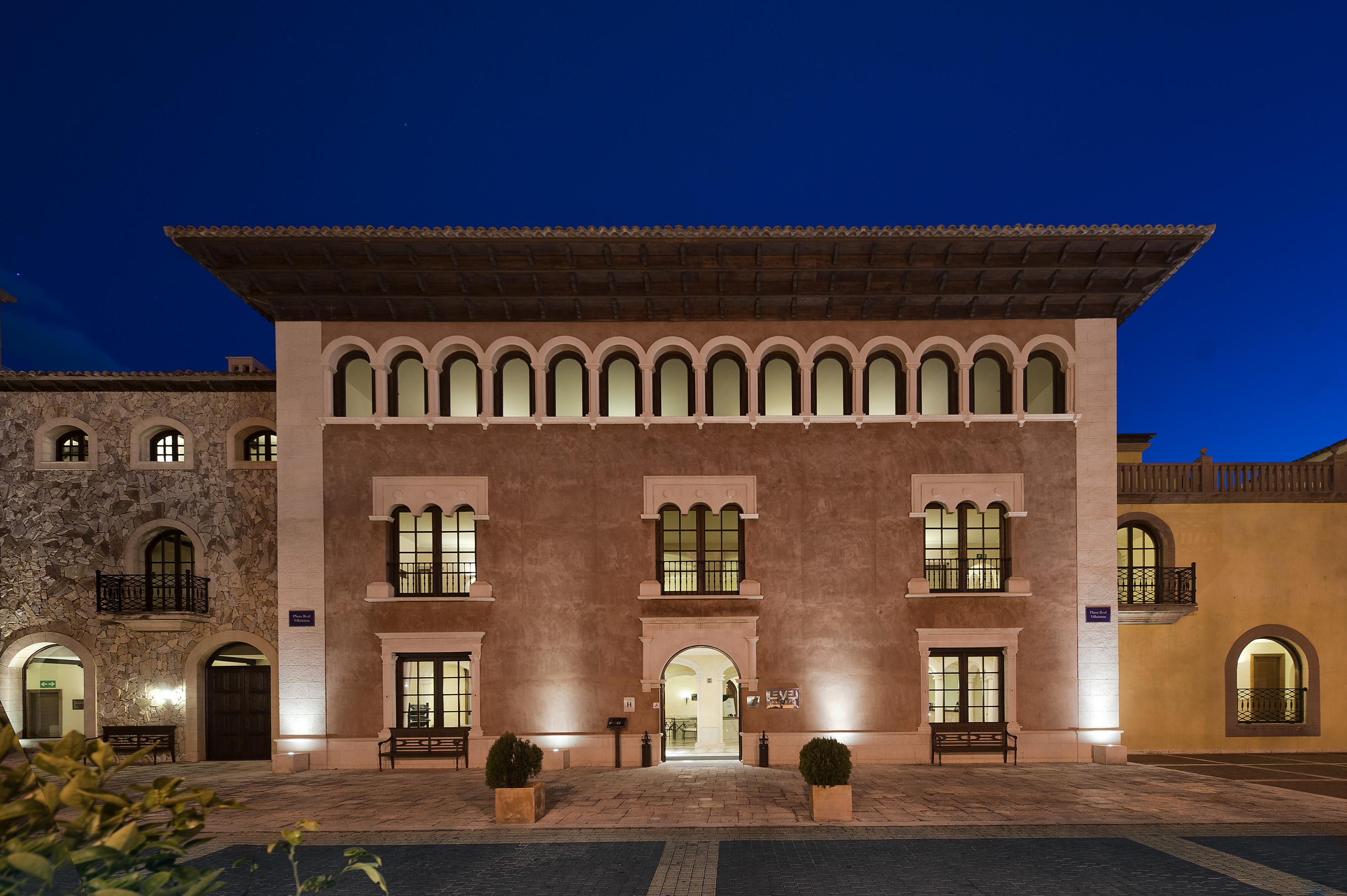 Mediterranean hotel facade at twilight with arched windows and warm lighting.