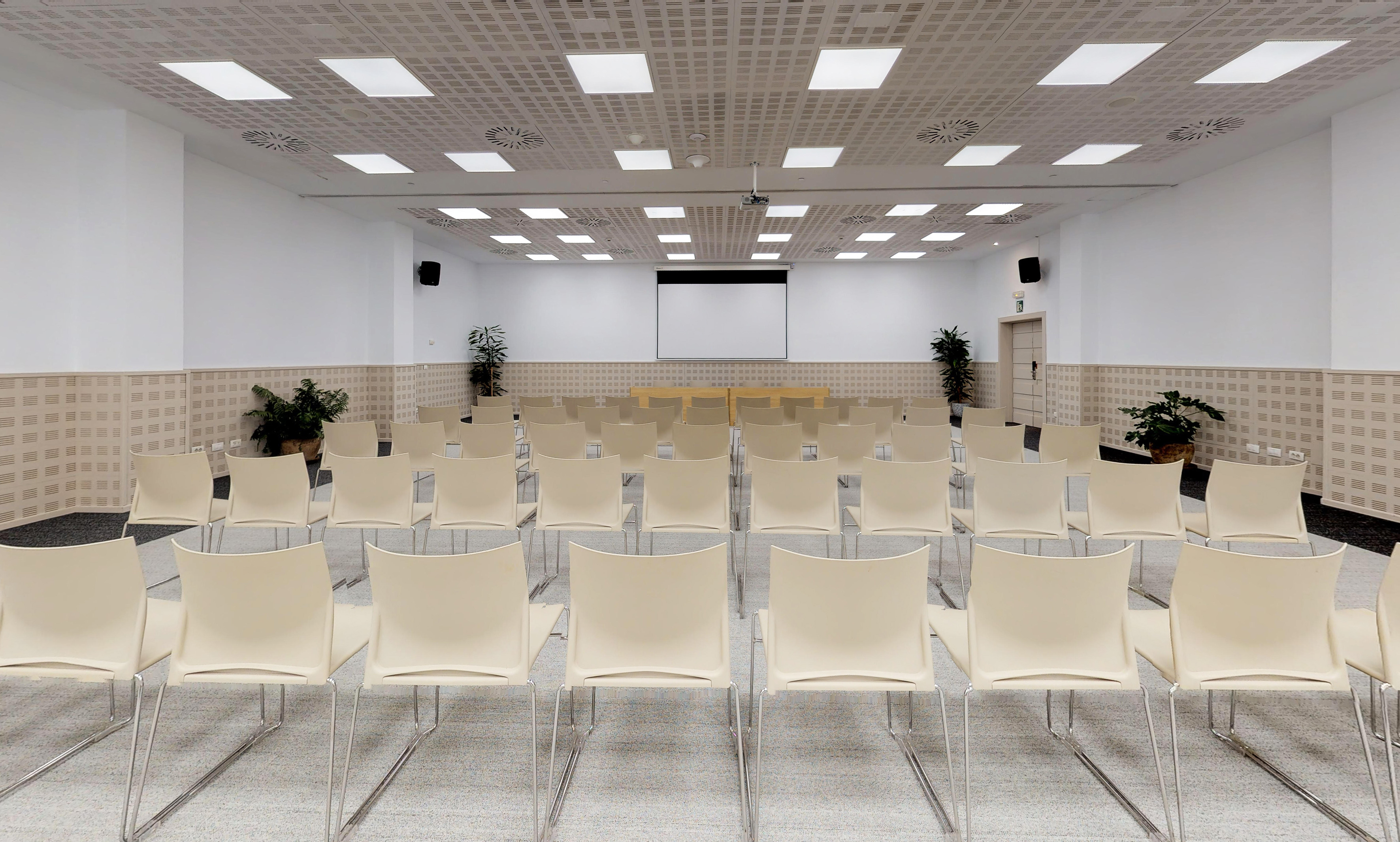 Empty modern conference room with rows of beige chairs and projection screen.