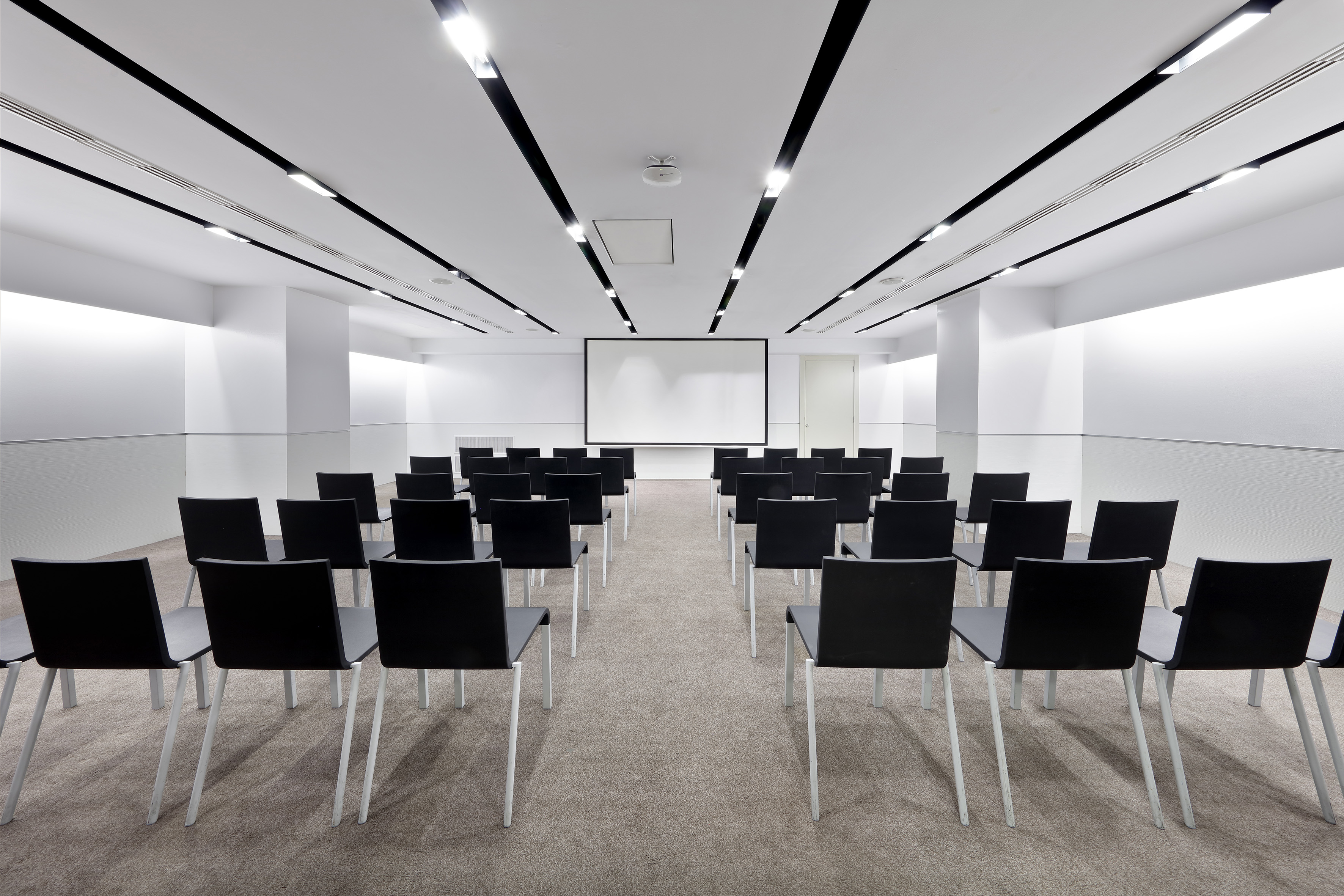 Empty modern conference room with black chairs and large projector screen.