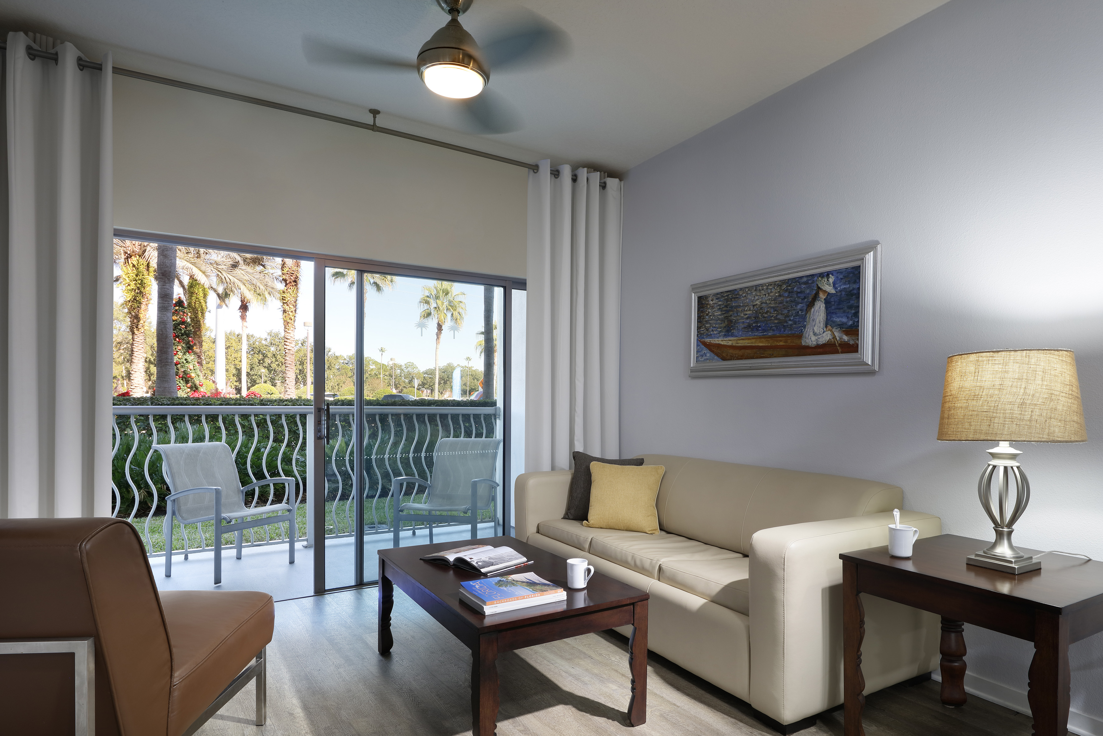 Modern living room with beige sofa, wood furniture, and balcony with tropical view.