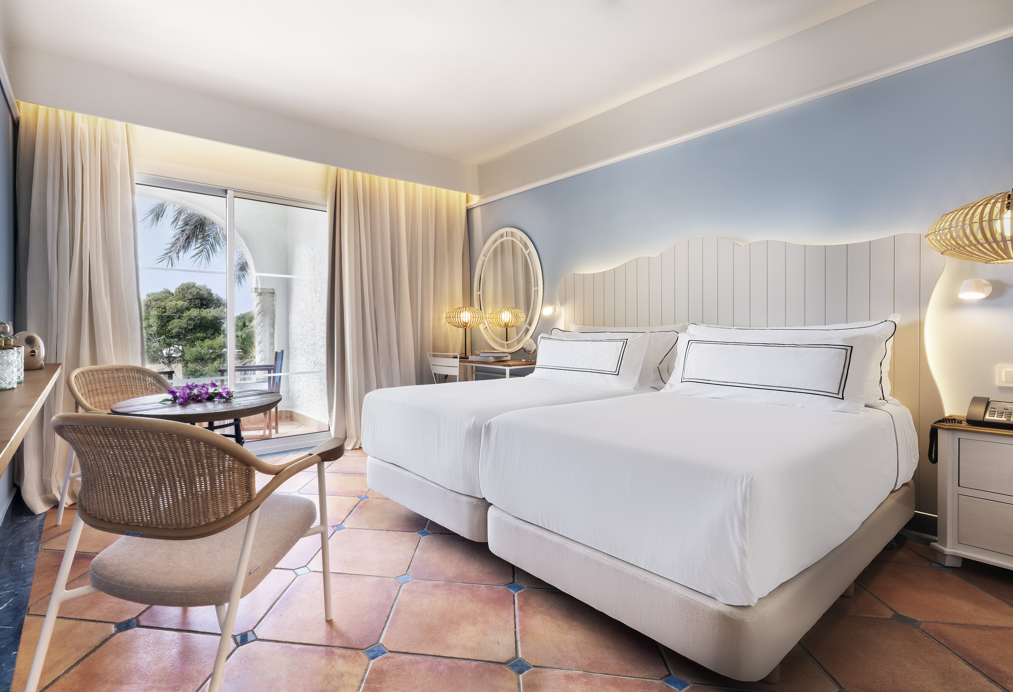 Resort room with twin beds, terracotta floor, and balcony access with palm trees.