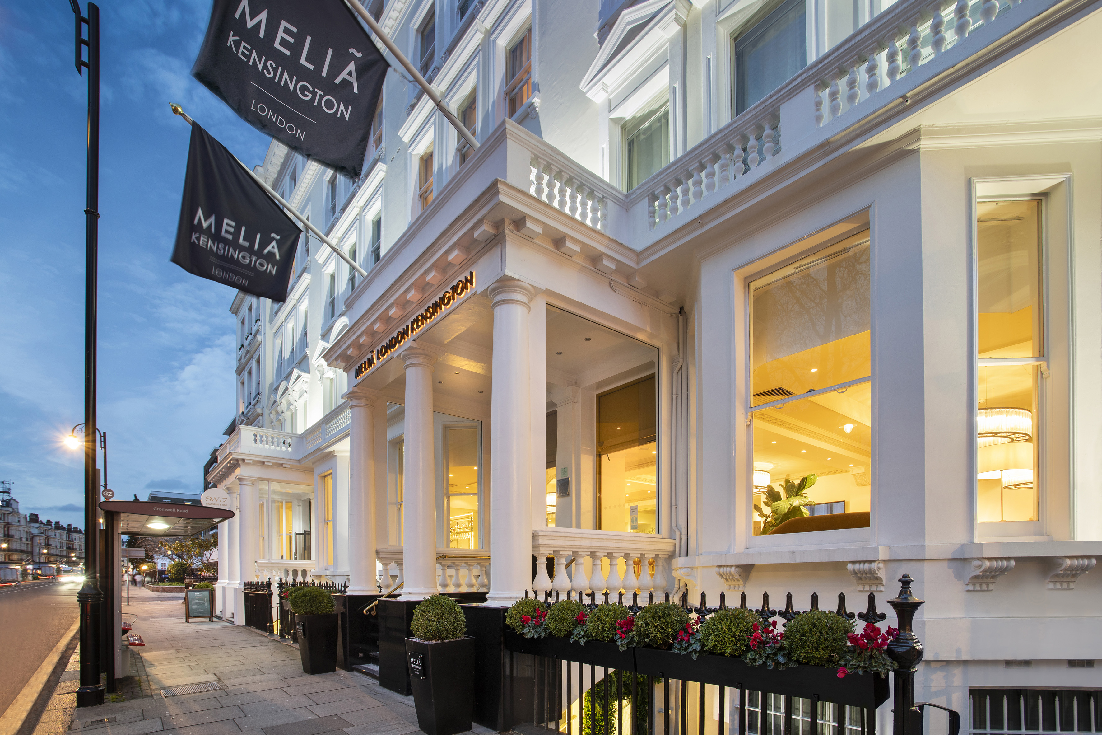 Meliá Kensington London hotel facade at dusk, with columns and flags.
