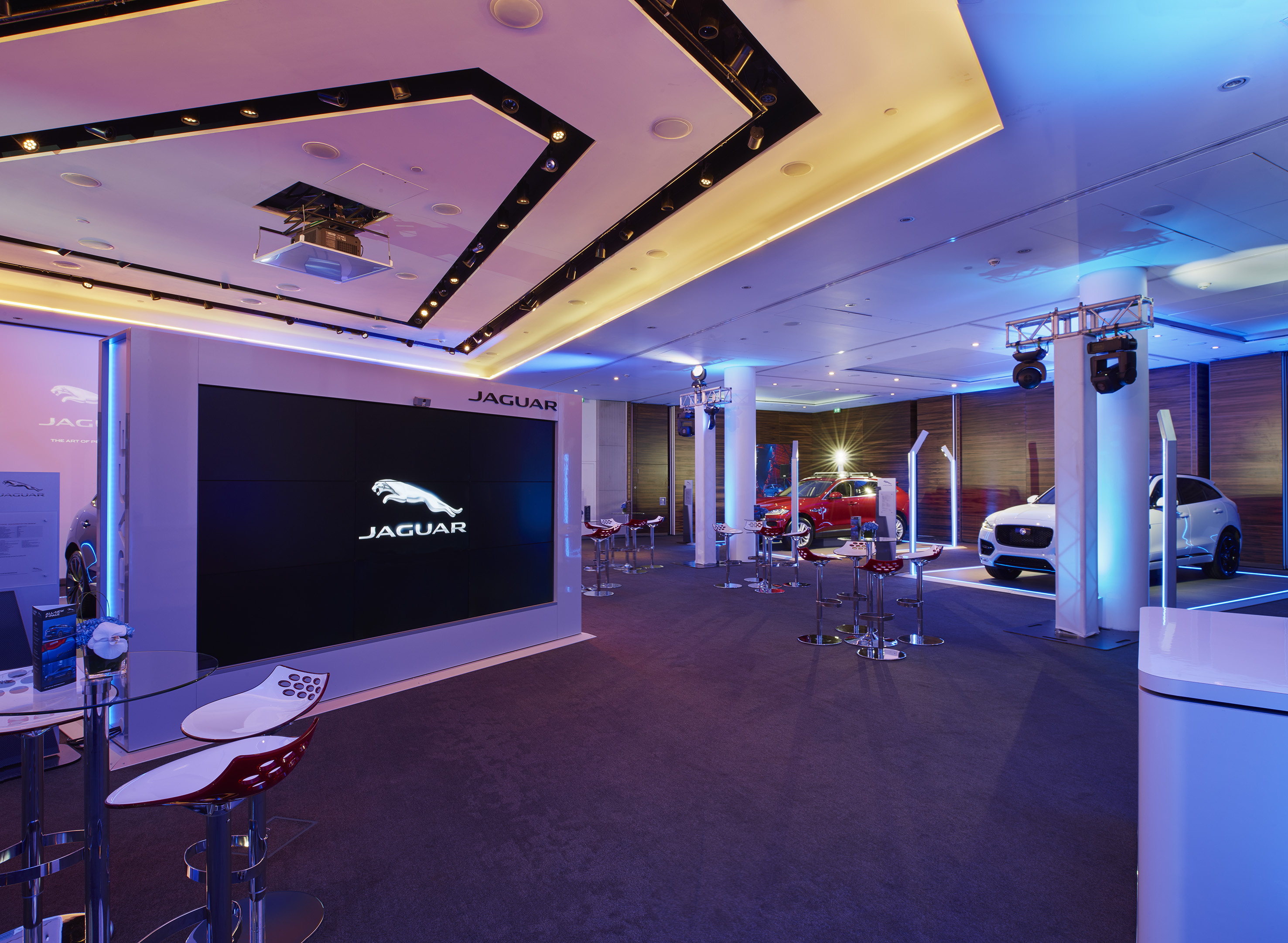 Jaguar car display featuring red and white SUVs, logo, and modern lighting.