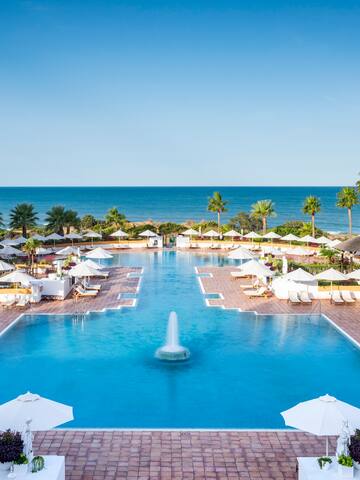 a pool with a fountain and umbrellas and palm trees