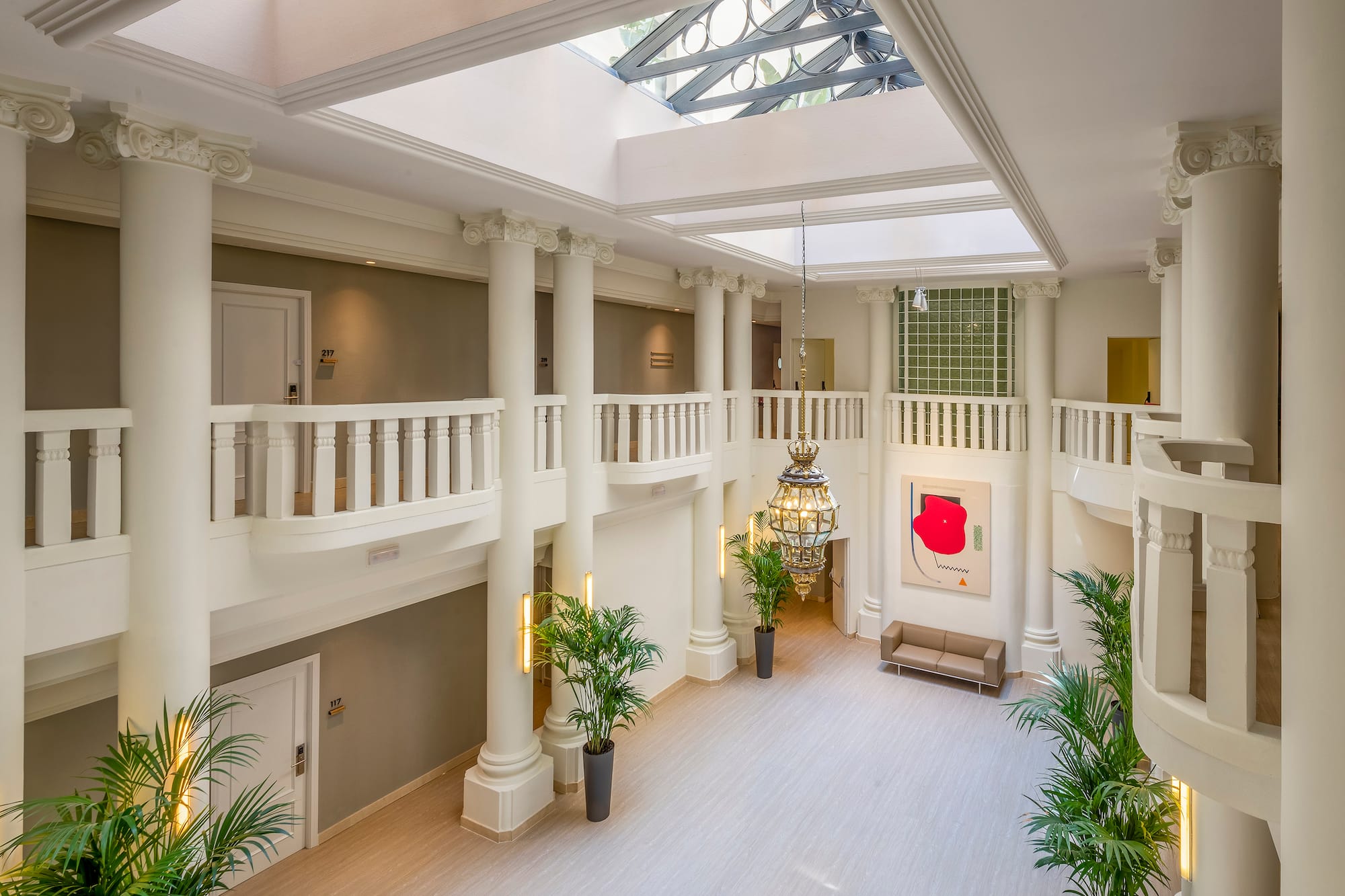 Elegant hotel atrium with classical columns, multi-level balconies, skylight, and chandelier.