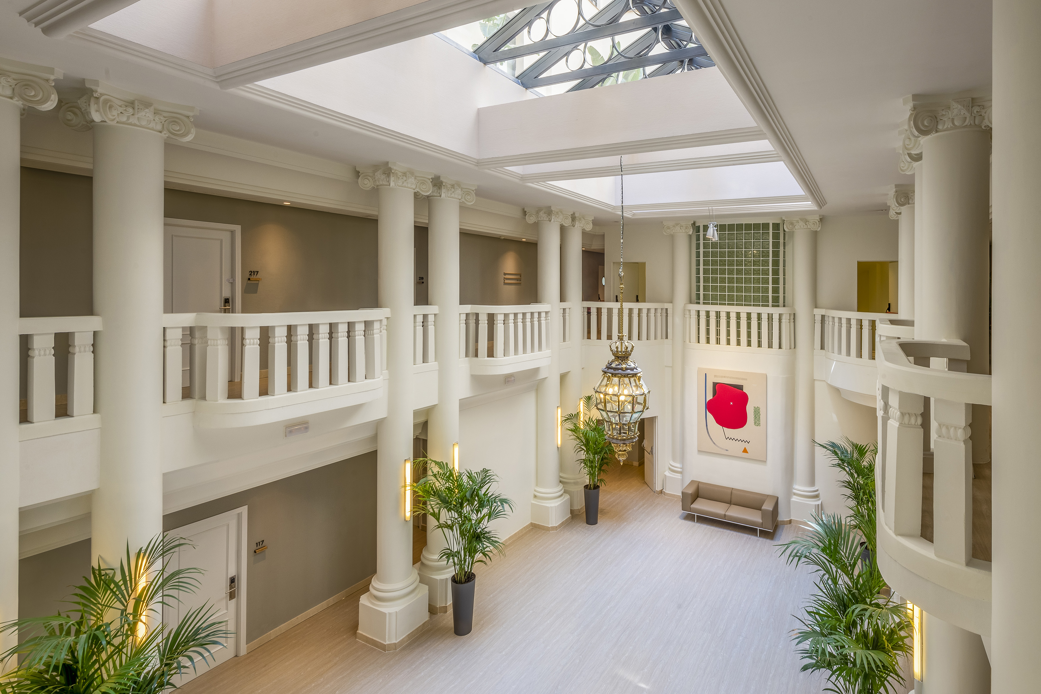 Elegant hotel atrium with classical columns, multi-level balconies, skylight, and chandelier.